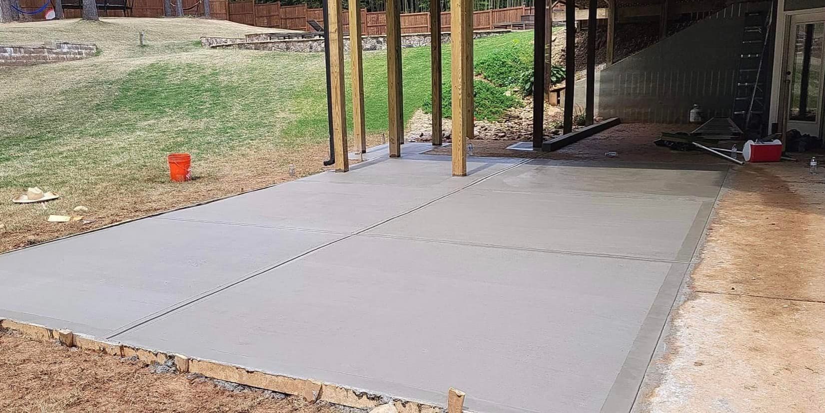 Freshly poured concrete patio with wooden supports and a grassy backyard.