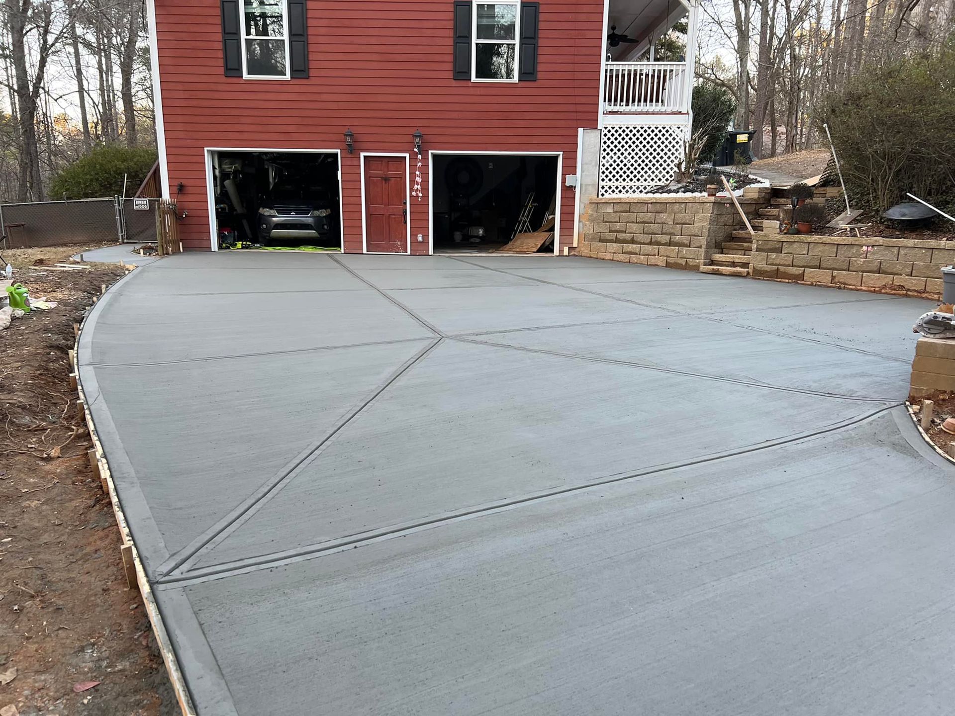 Newly poured gray concrete driveway with decorative scoring lines in front of a red house with a two-car garage.