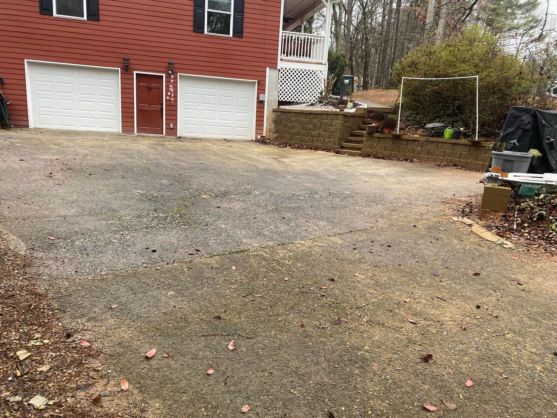 Gravel driveway in front of a brick house with two garage doors and a small retaining wall.