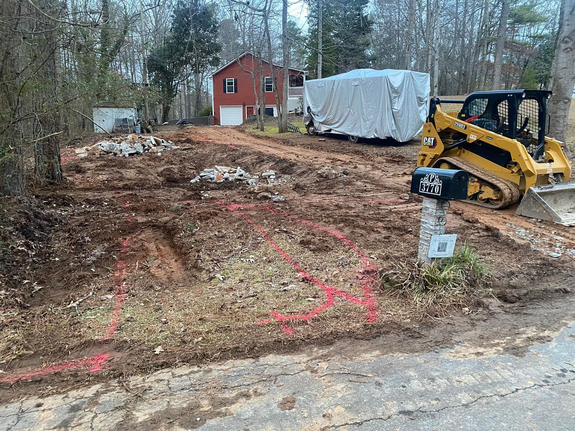A construction site with a skid steer, marked ground, and a house in the background.