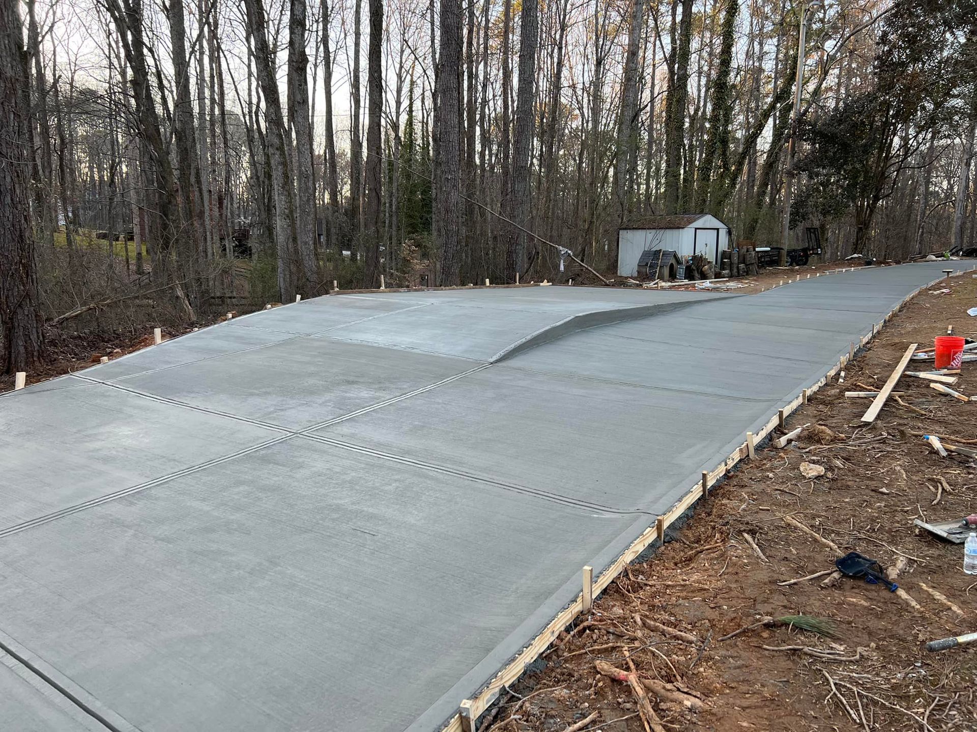 Freshly poured concrete driveway with wooden formwork in a wooded area.