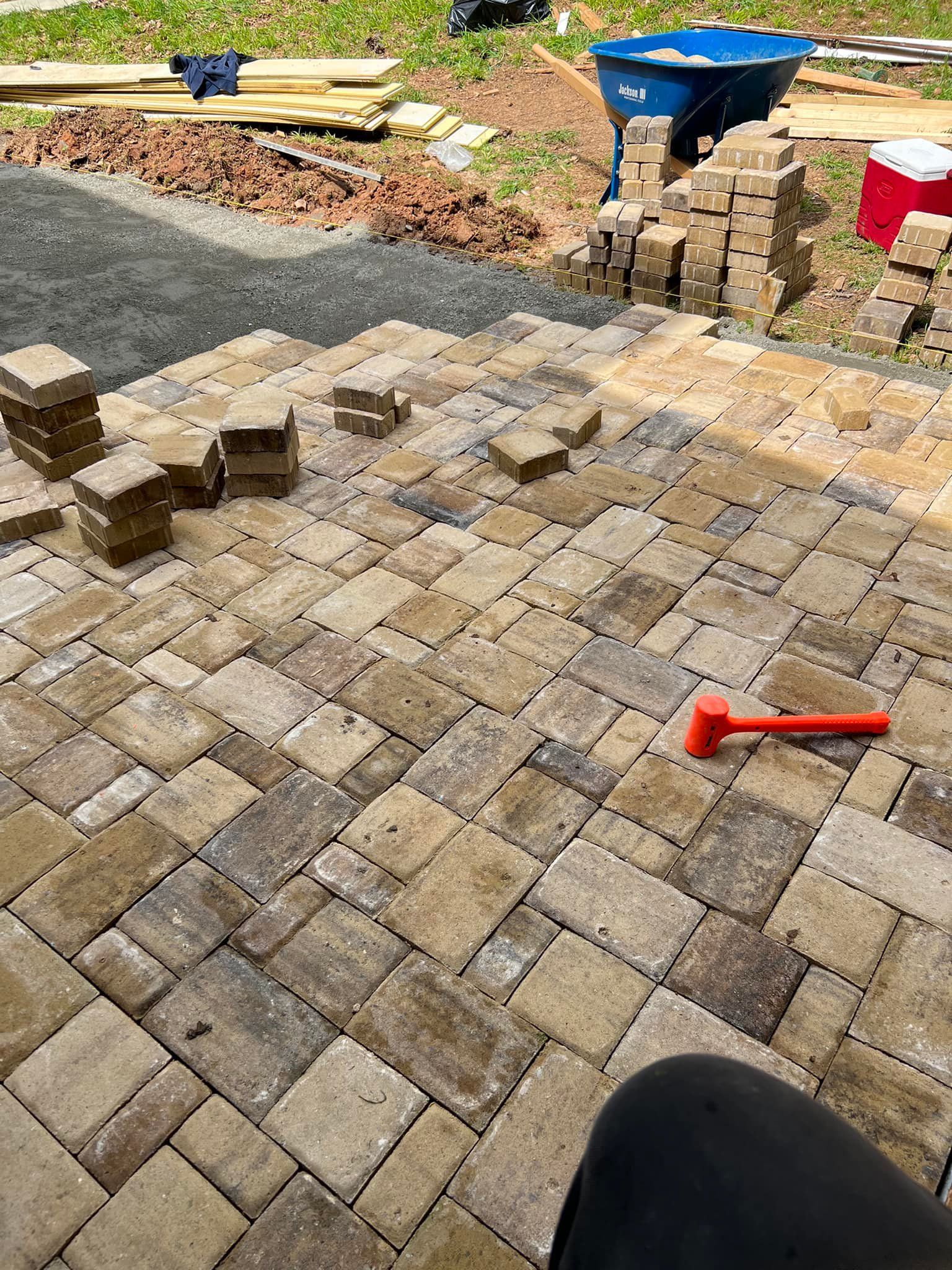 Construction of a stone patio: blocks being laid out with a mallet on a gravel base. Various tan/brown colors.
