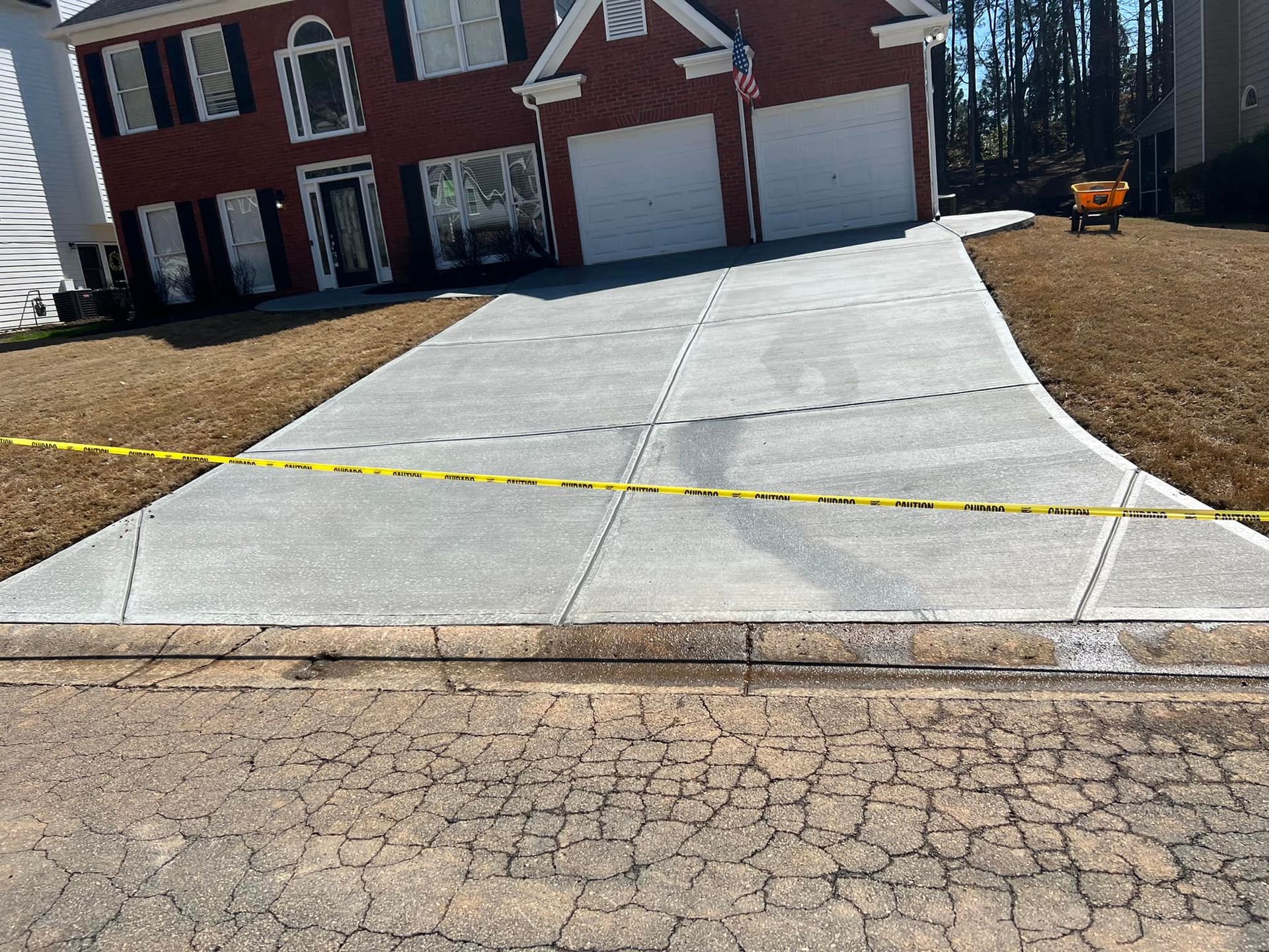 New concrete driveway in front of a brick house; yellow caution tape across the driveway's surface.