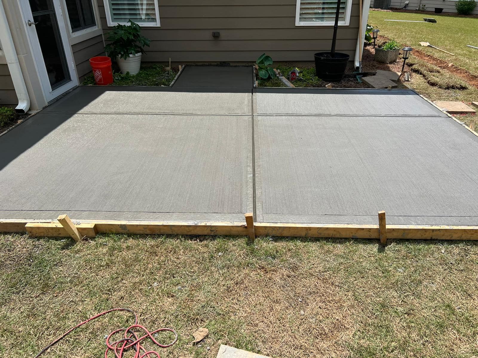 Newly poured concrete patio, bordered by wooden framing, sits on grass.
