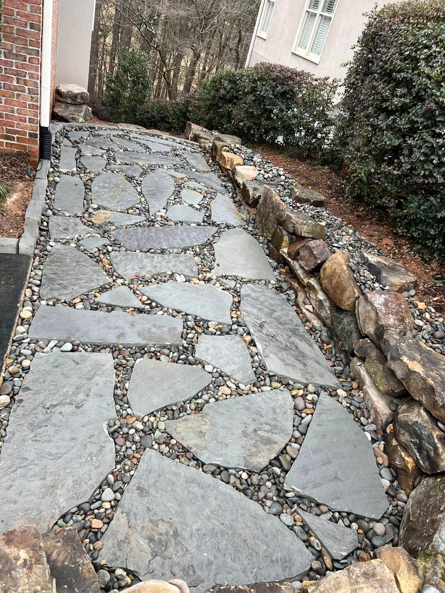Stone pathway with irregular-shaped pavers and small rock infill, next to a stone retaining wall.