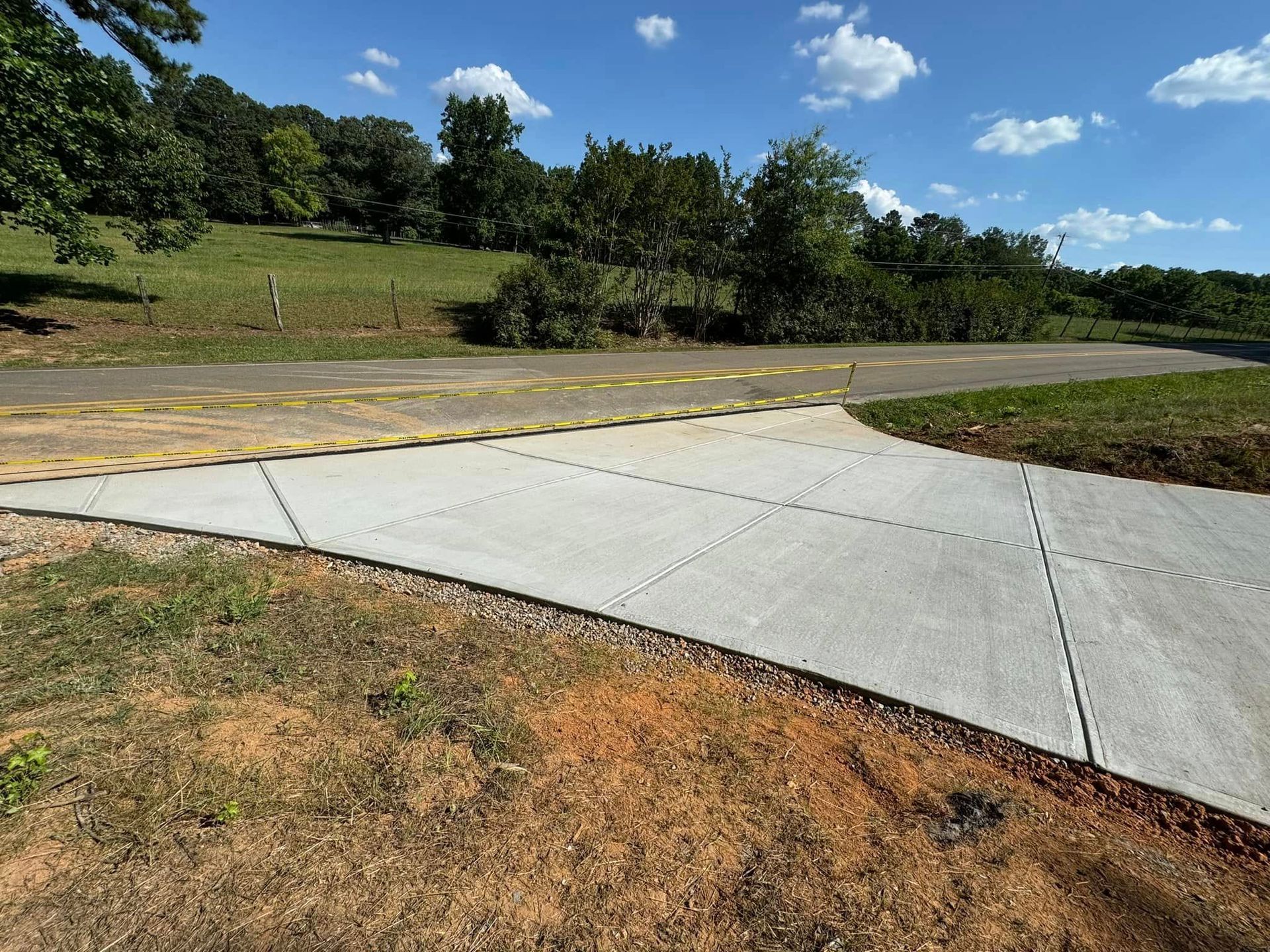 Concrete pathway splitting; a paved road with yellow bumps leads into the trees.