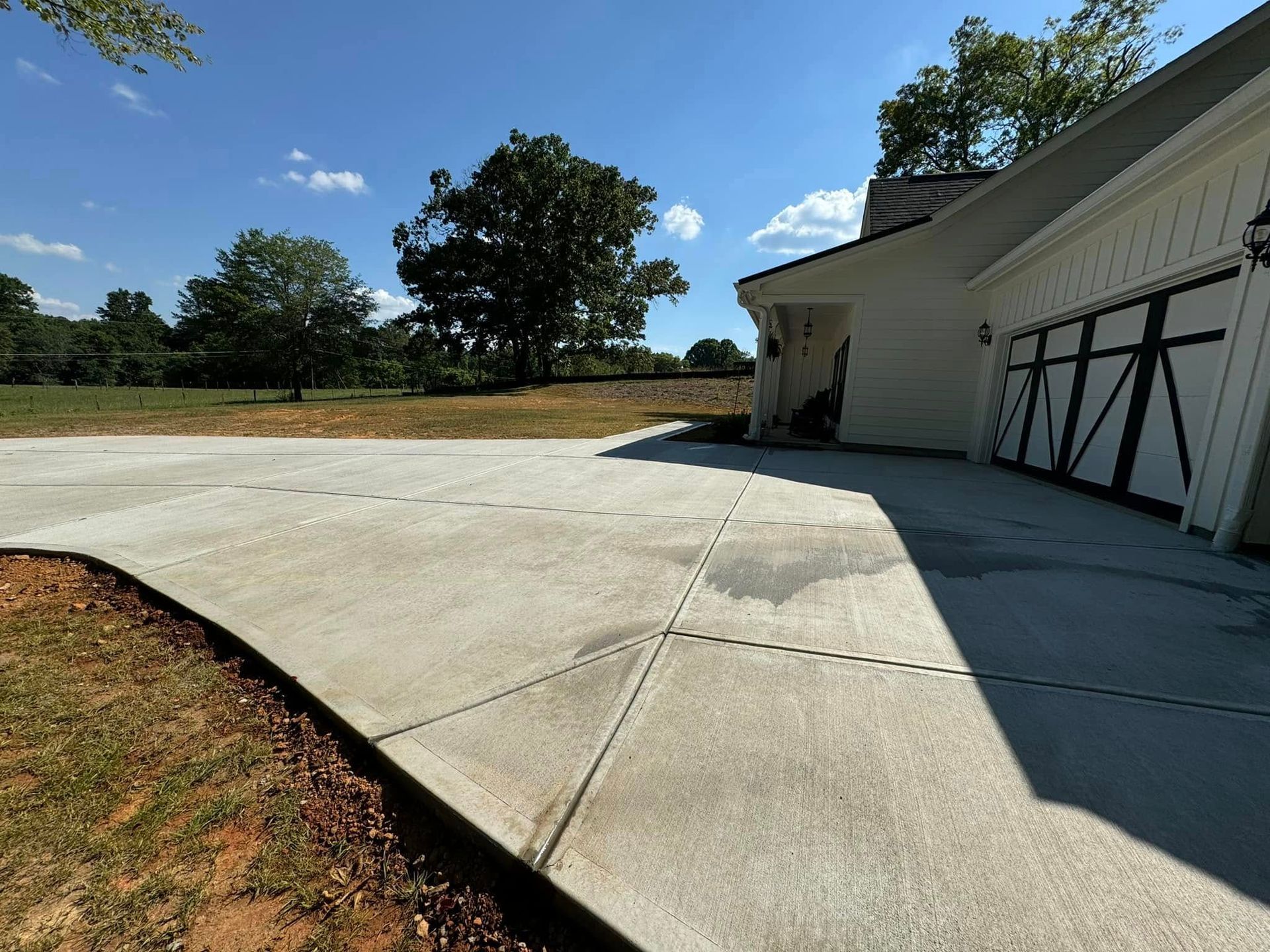 Newly poured concrete driveway with a house and trees on a sunny day.