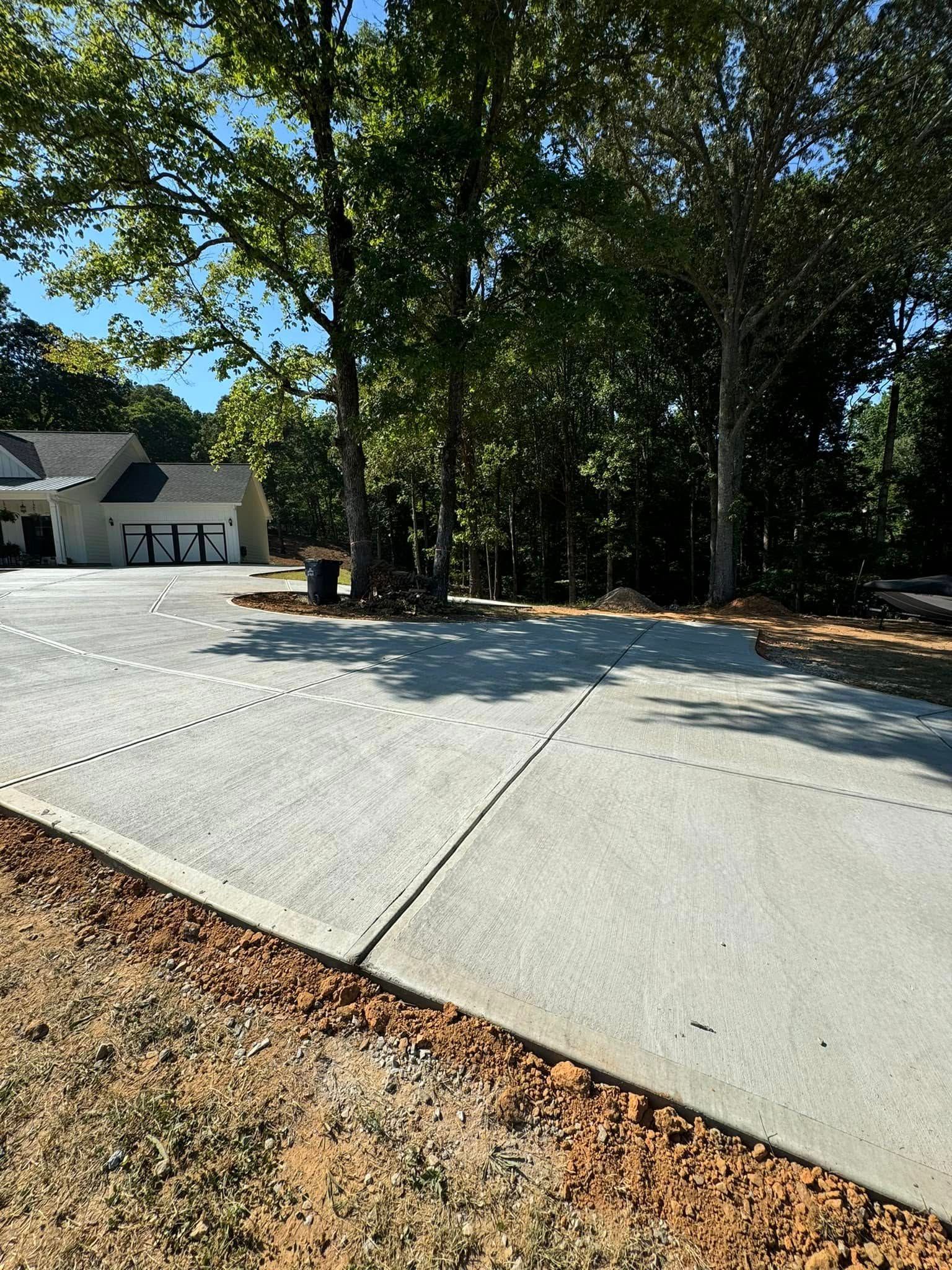 Newly poured concrete driveway with brown border, trees, and house in the background.