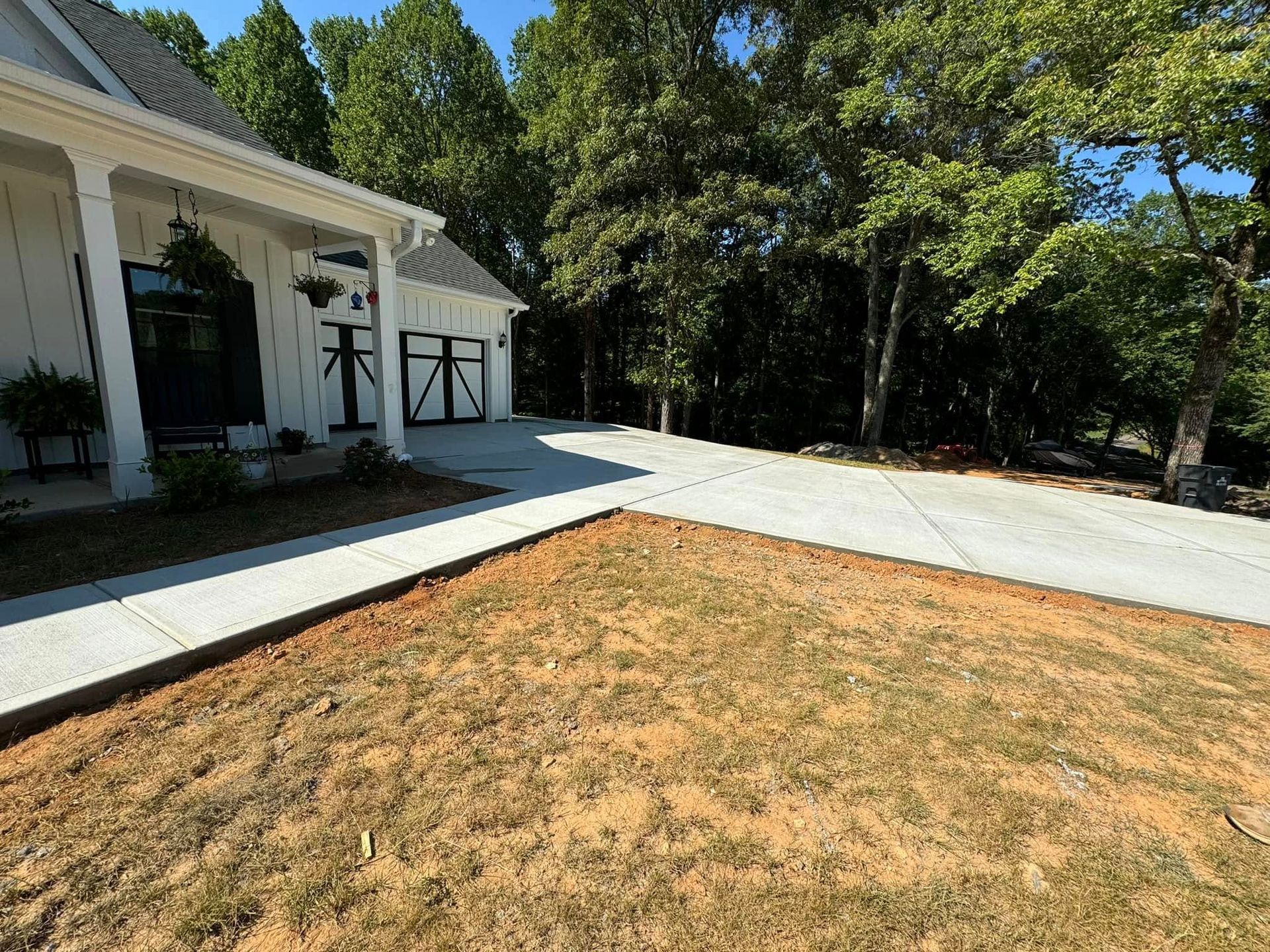 White house with concrete driveway and dry, brown yard. Trees in background.