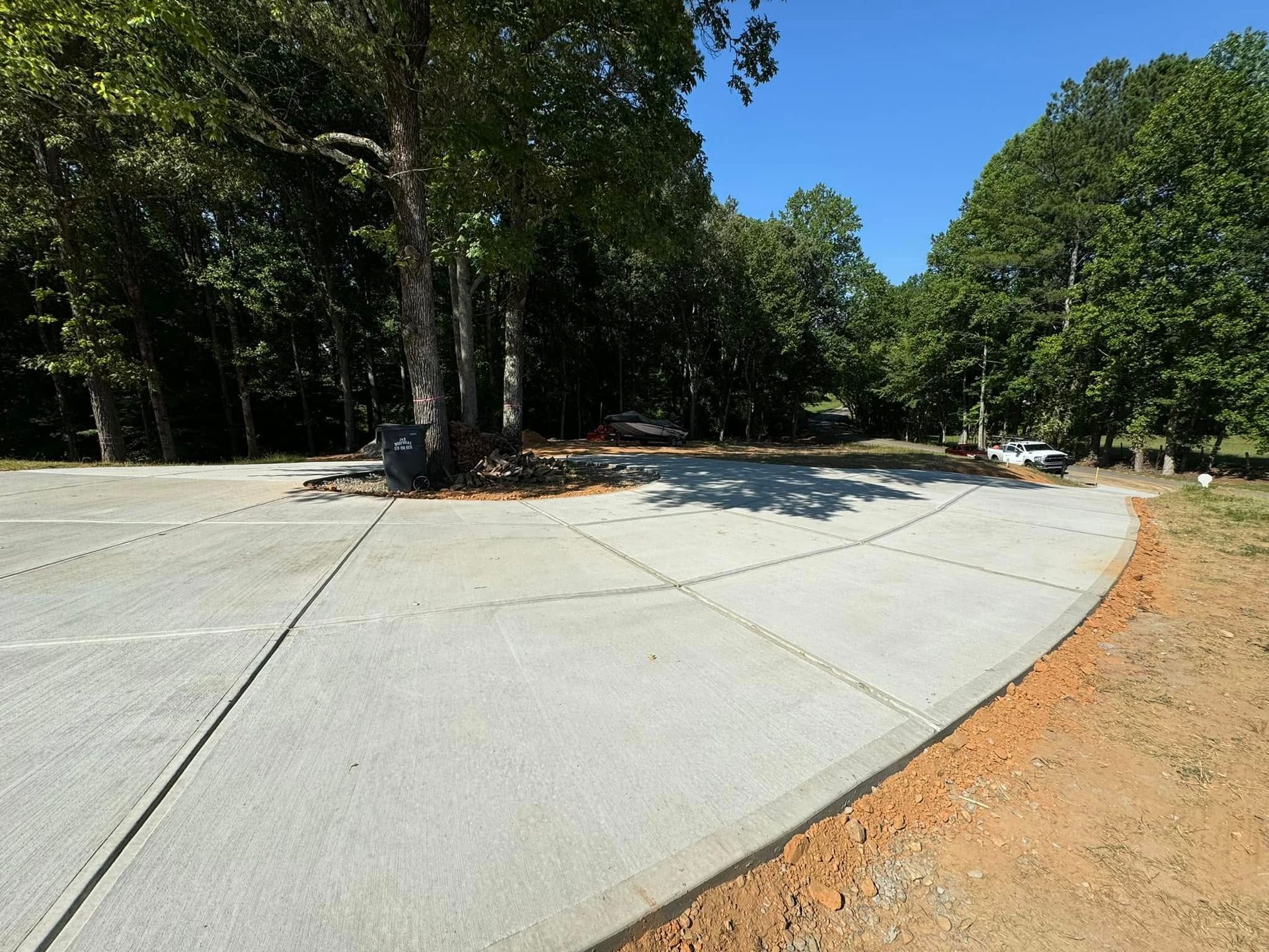 New concrete parking area in a wooded area with trees and blue sky.