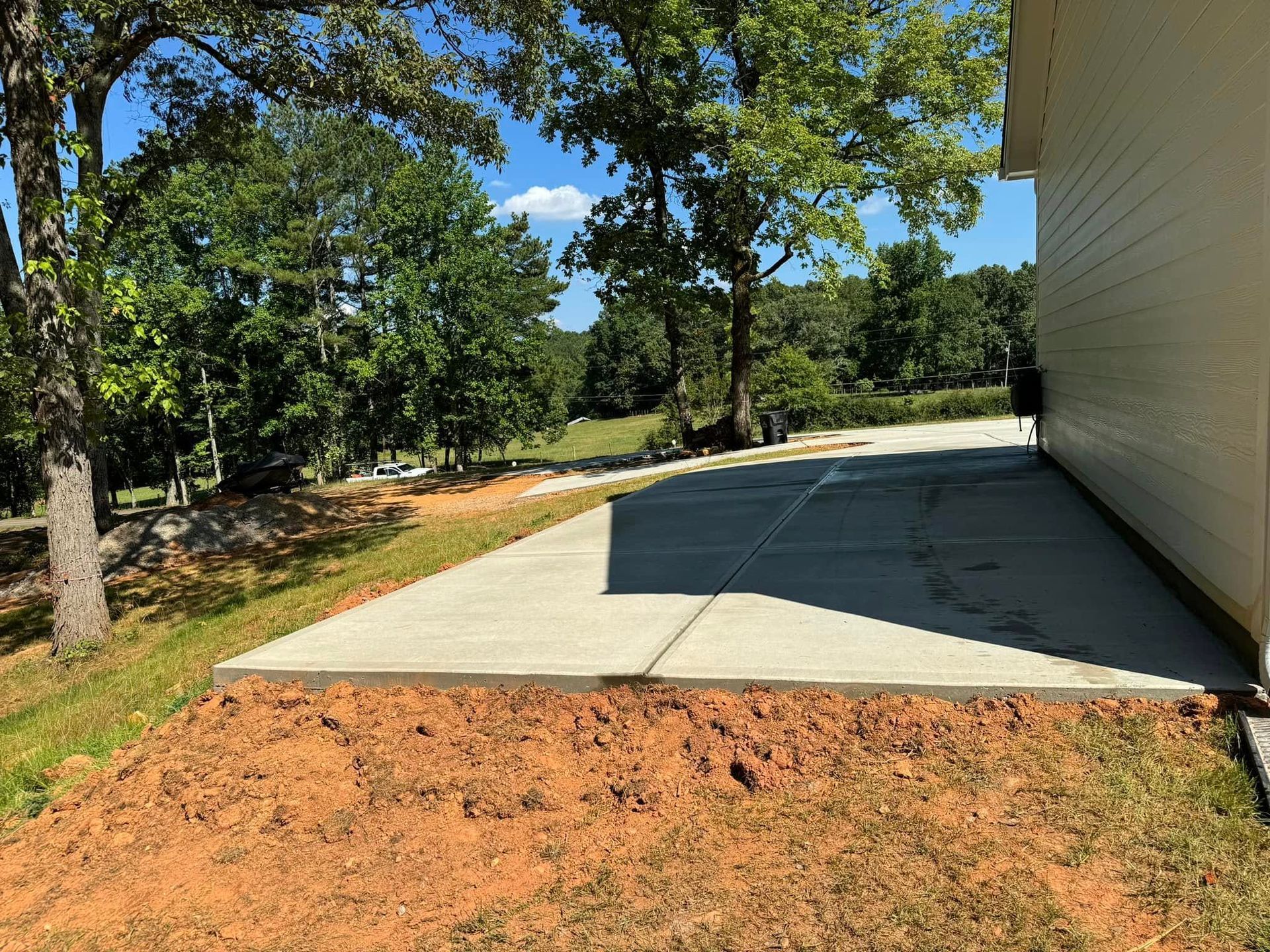 Concrete patio next to a building, bordered by dirt and grass, with trees in the background.
