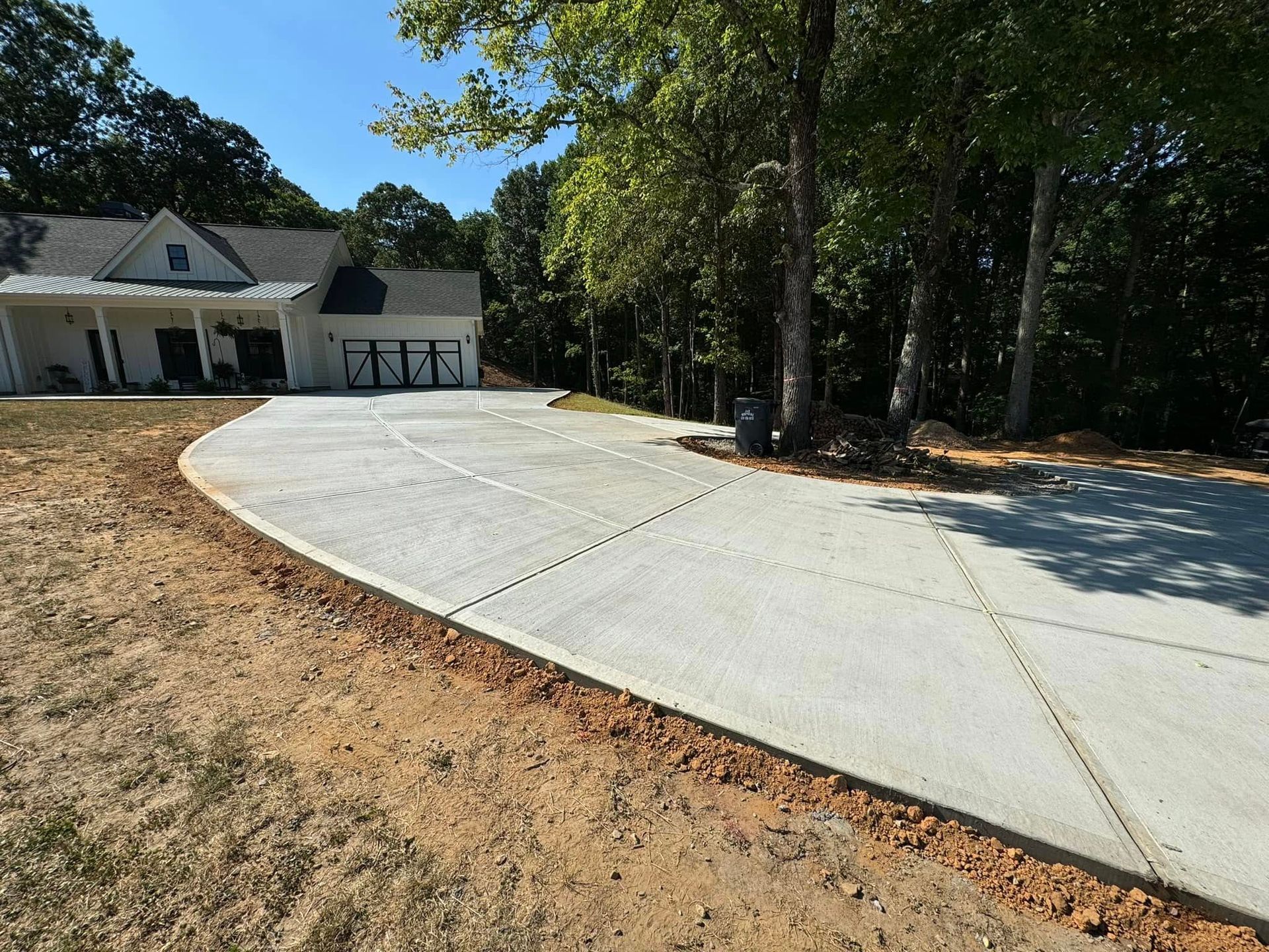Concrete driveway leading to a house with a white exterior and a garage, surrounded by trees.
