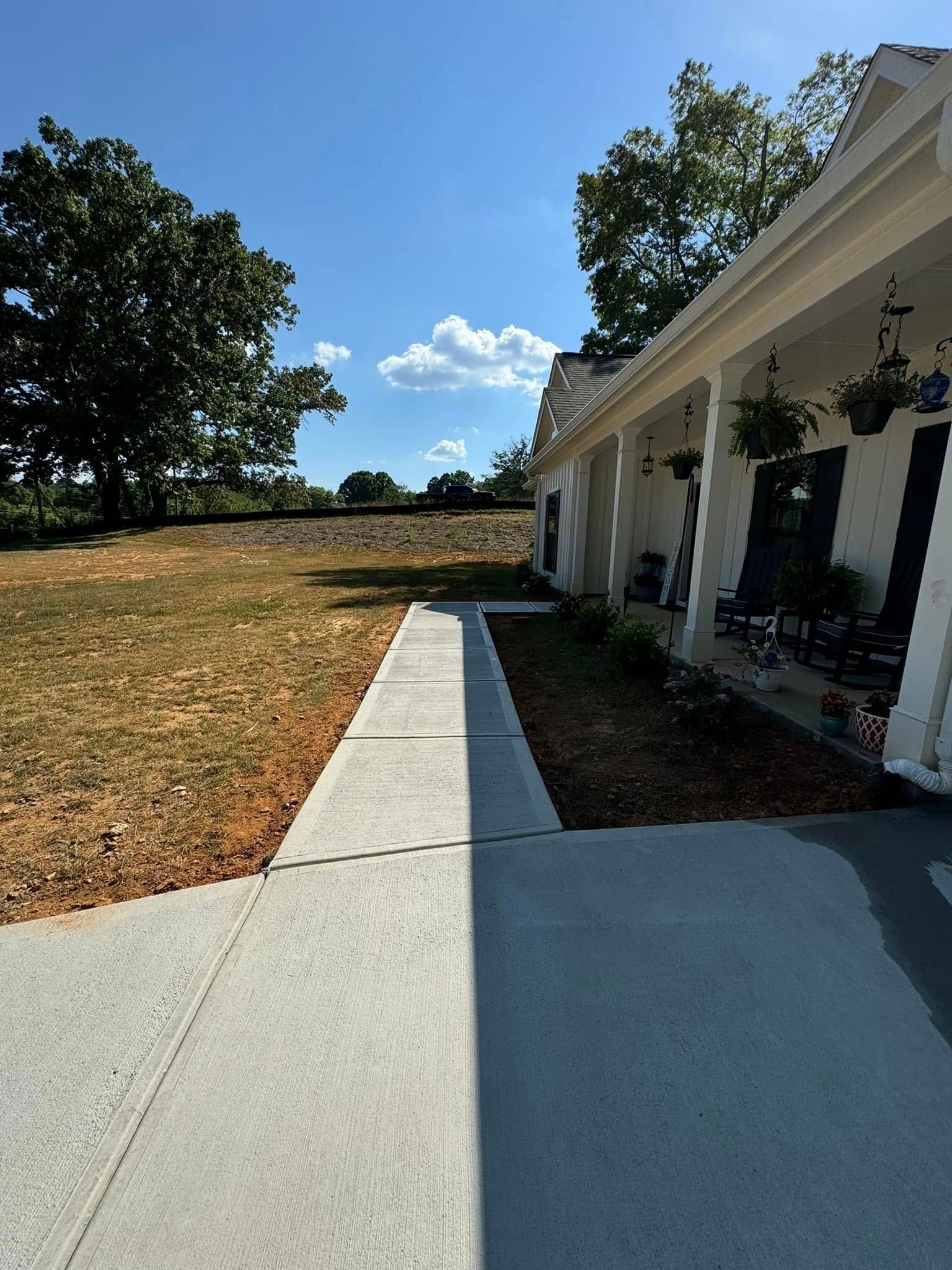 Concrete path leading to a white house with hanging plants under a blue sky, sunny day.