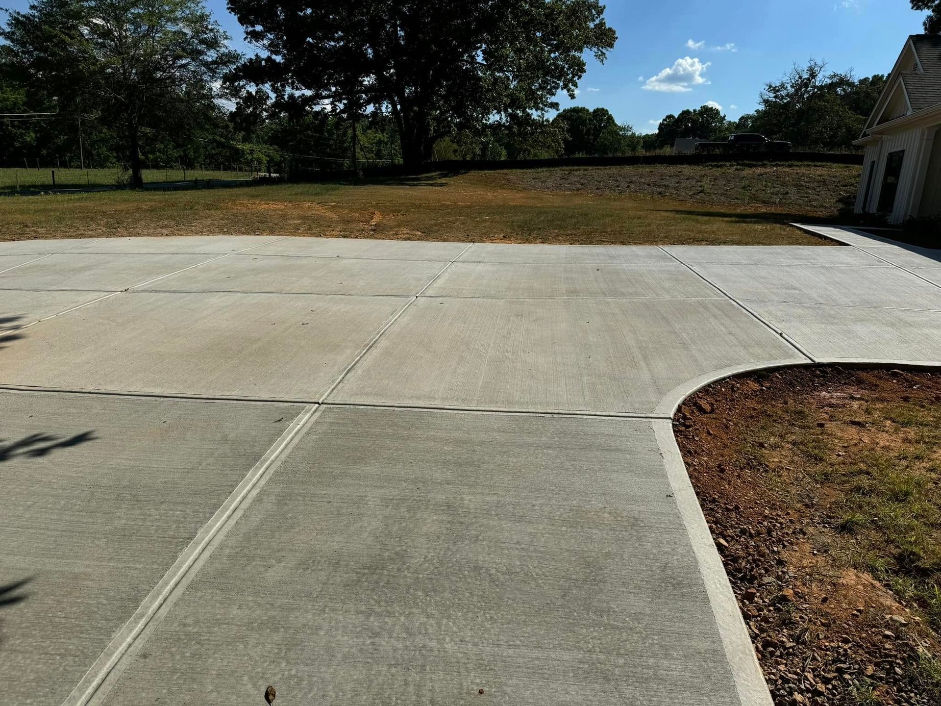 Concrete driveway curving to the right, adjacent to brown mulch and green grass, with trees in the background.