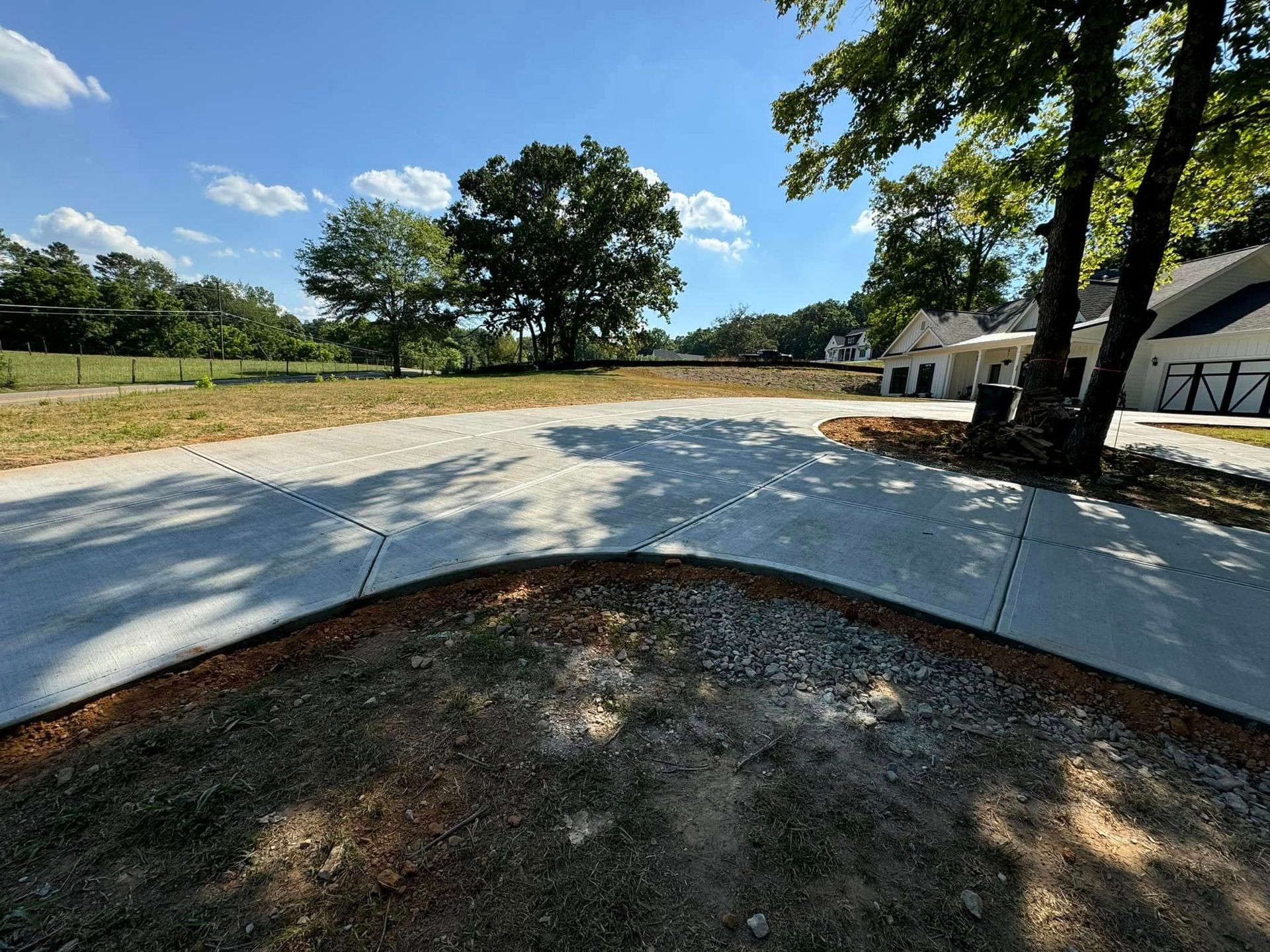 A paved driveway curves around a grassy area with trees, leading to a modern white building on a sunny day.