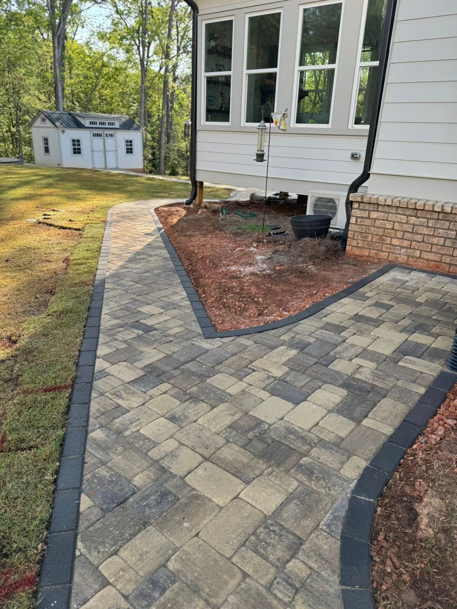 Paver walkway in a yard, leading to a house and shed. Walkway is bordered by dark pavers.