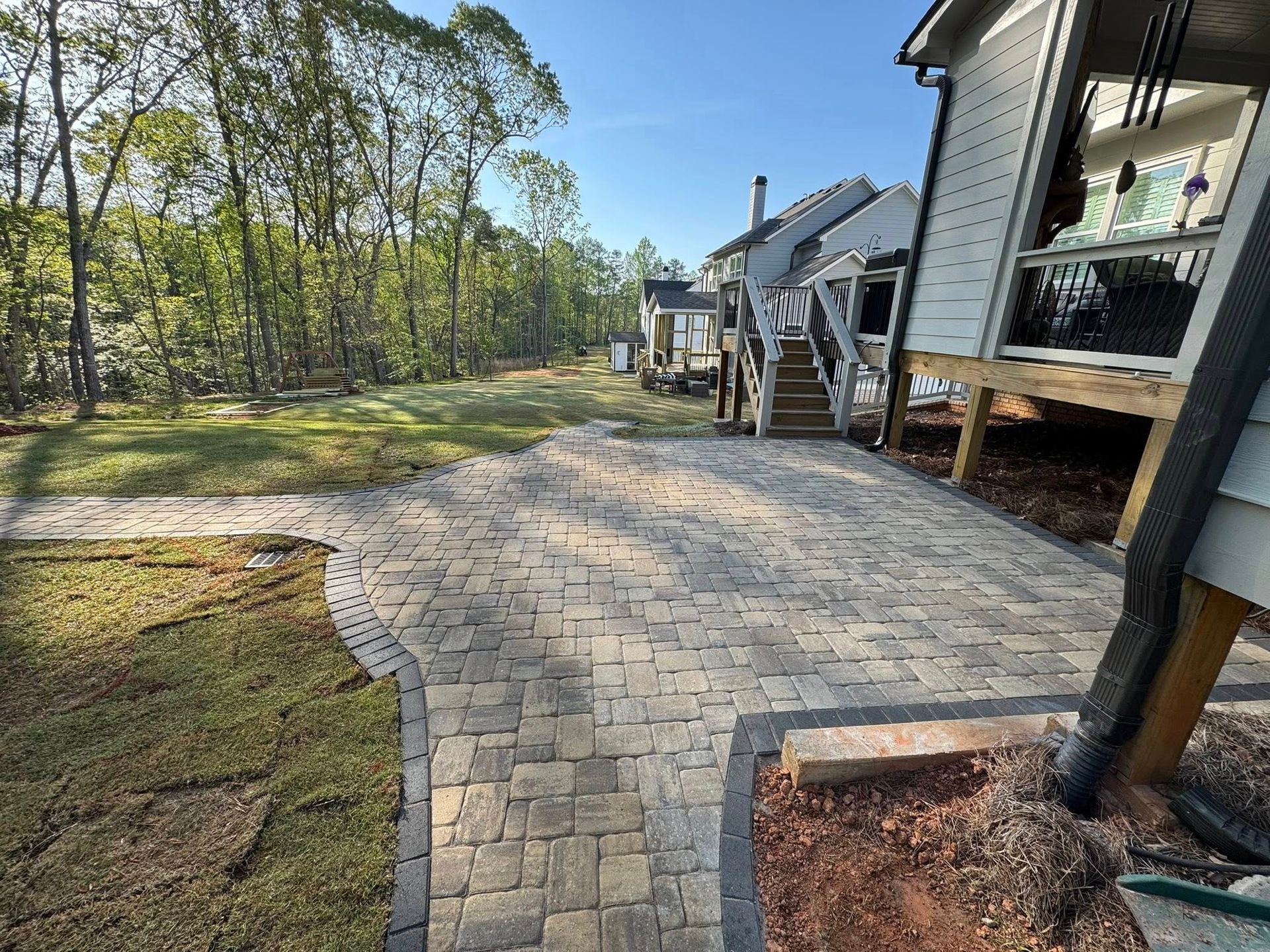 Brick patio next to a house with steps leading up to a deck. Trees are in the background.