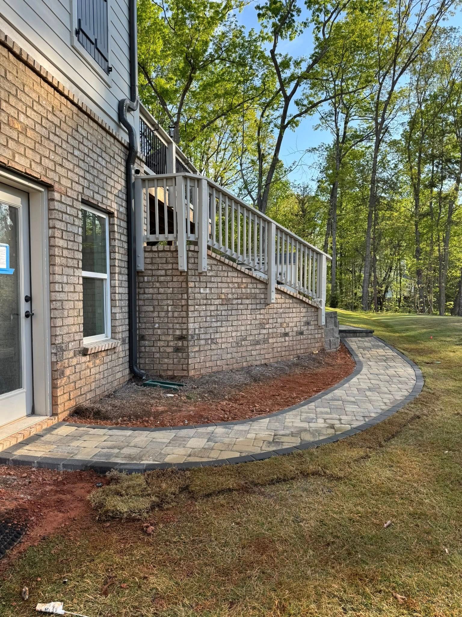 Brick house exterior with a curved stone path, stairs, and railing leading to a deck.