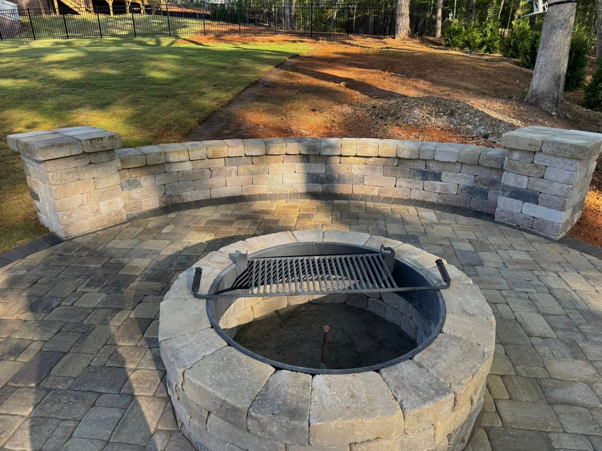 Stone fire pit with grill and curved stone seating in a backyard setting.