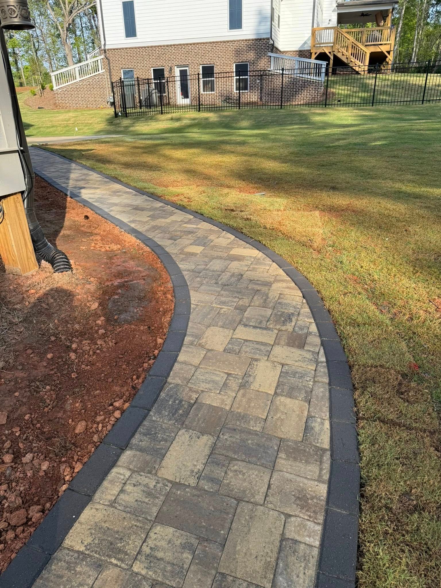 Curving brick path with dark border, leading through a grassy yard, house in the background.