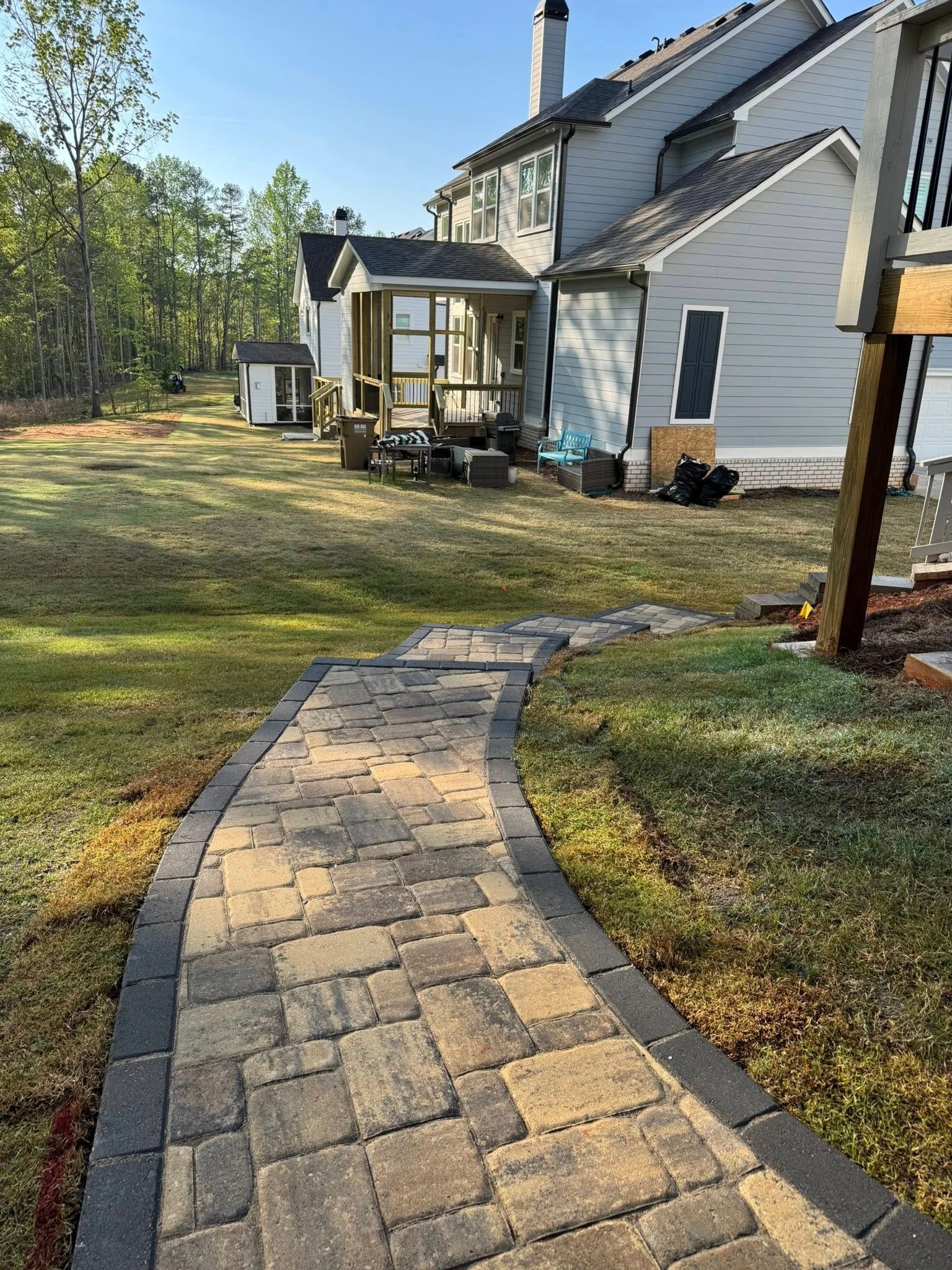 Stone pathway leading to a house with a yard. A shed and patio are in the distance.
