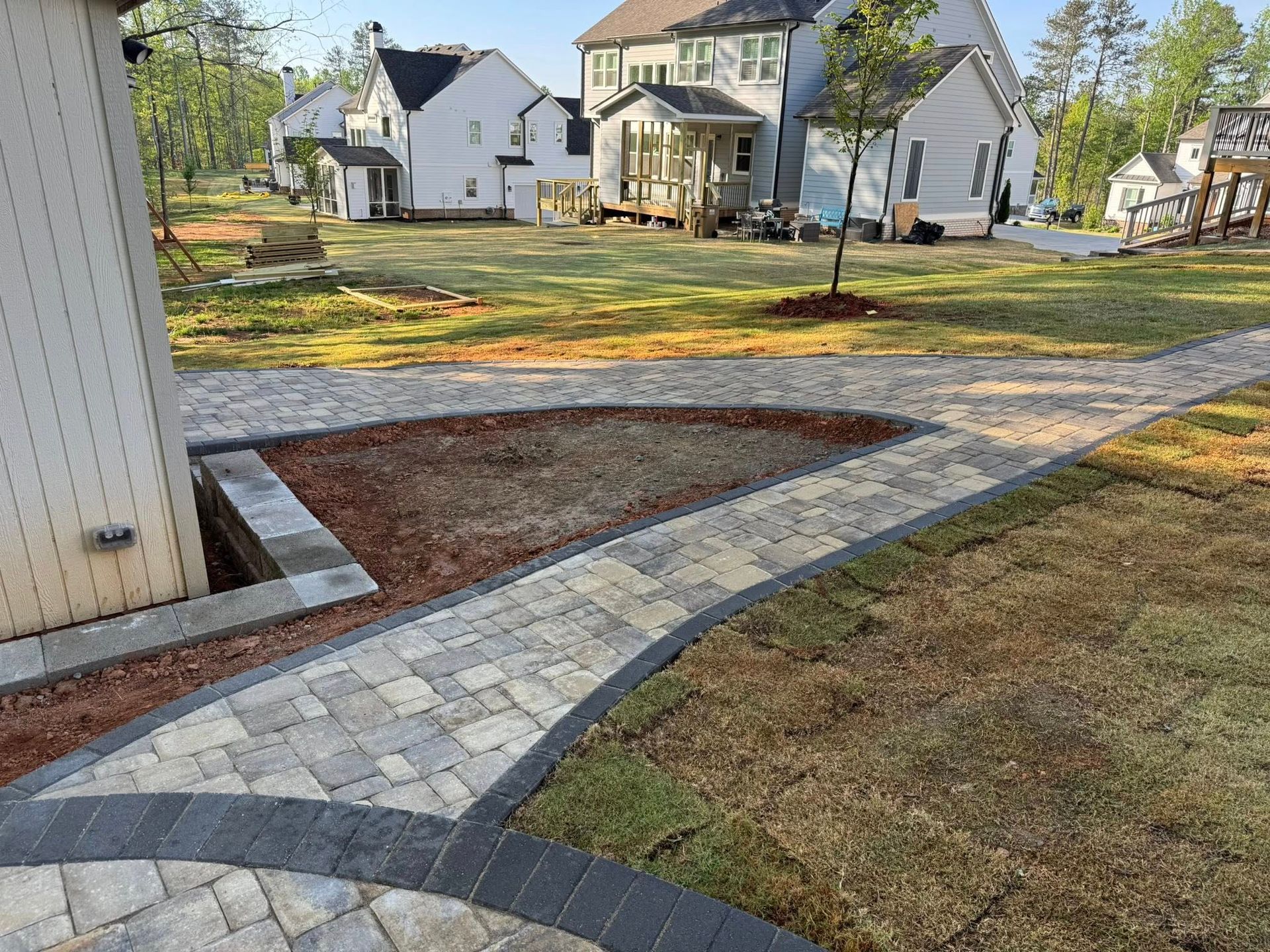 Stone pathway curves through a yard with houses in the background. Grass and red mulch surround the path.
