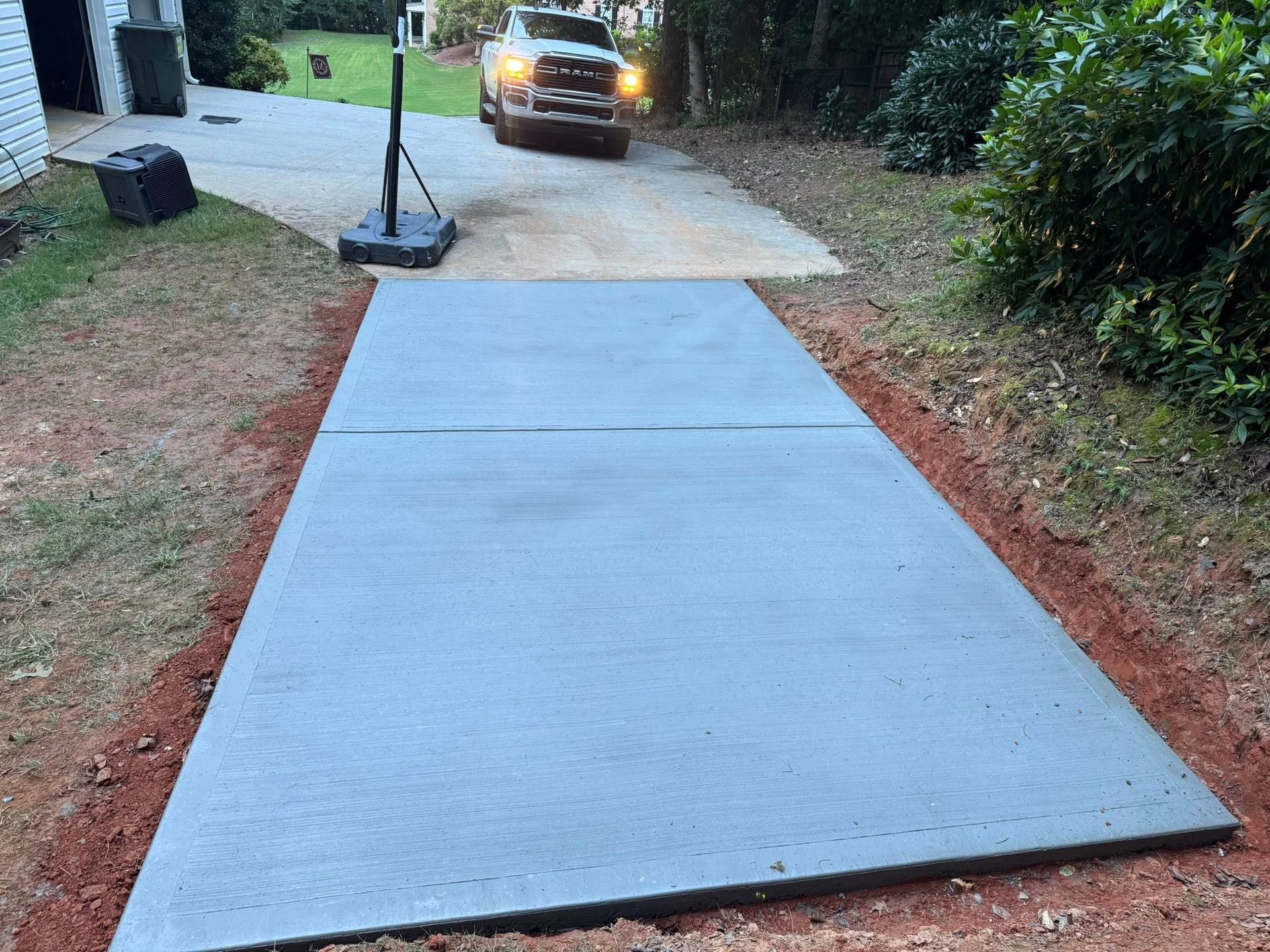 Newly poured concrete pad for basketball hoop; pickup truck in background.