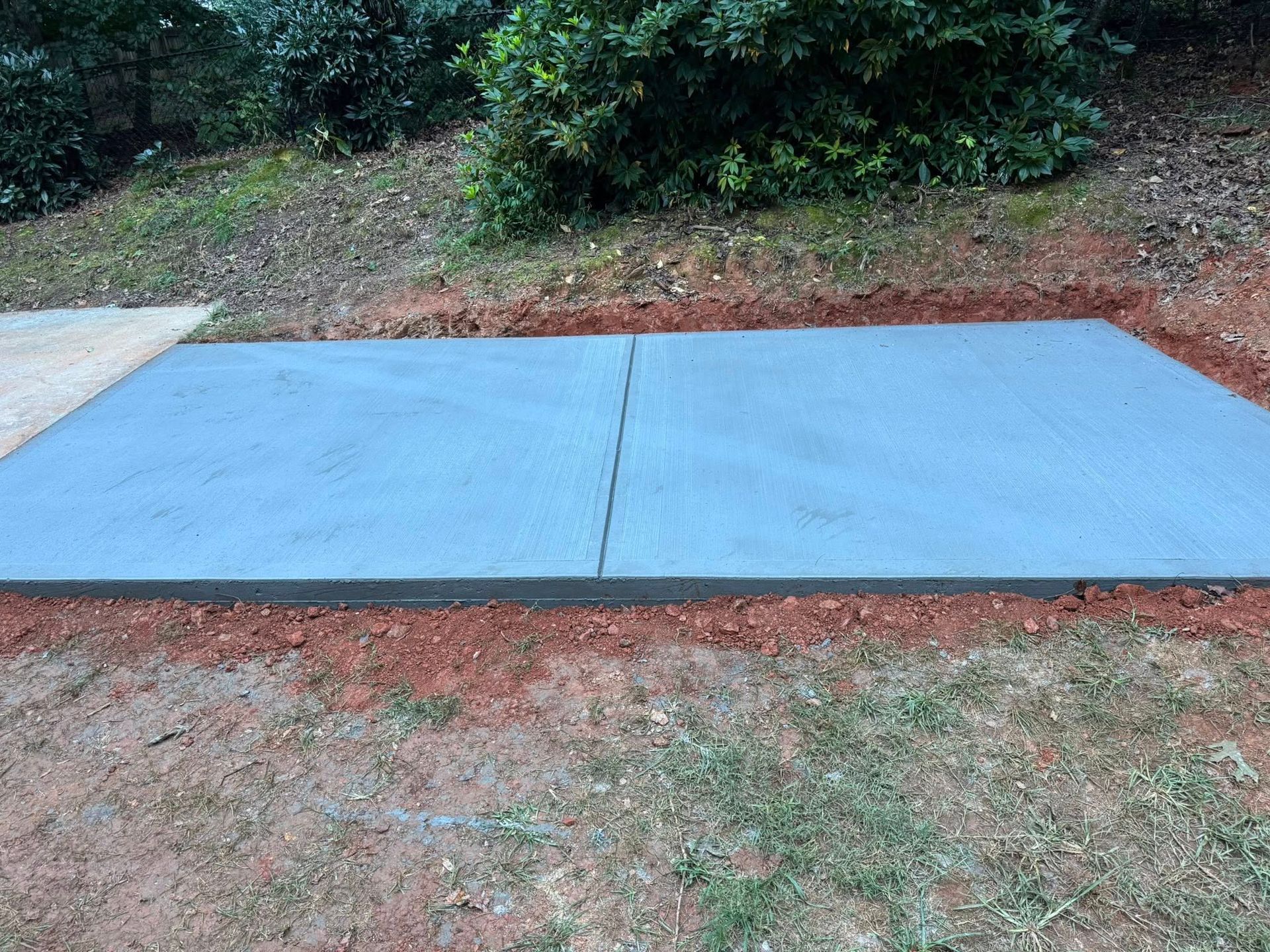 Concrete slab, split down the middle, on reddish dirt, with foliage in the background.