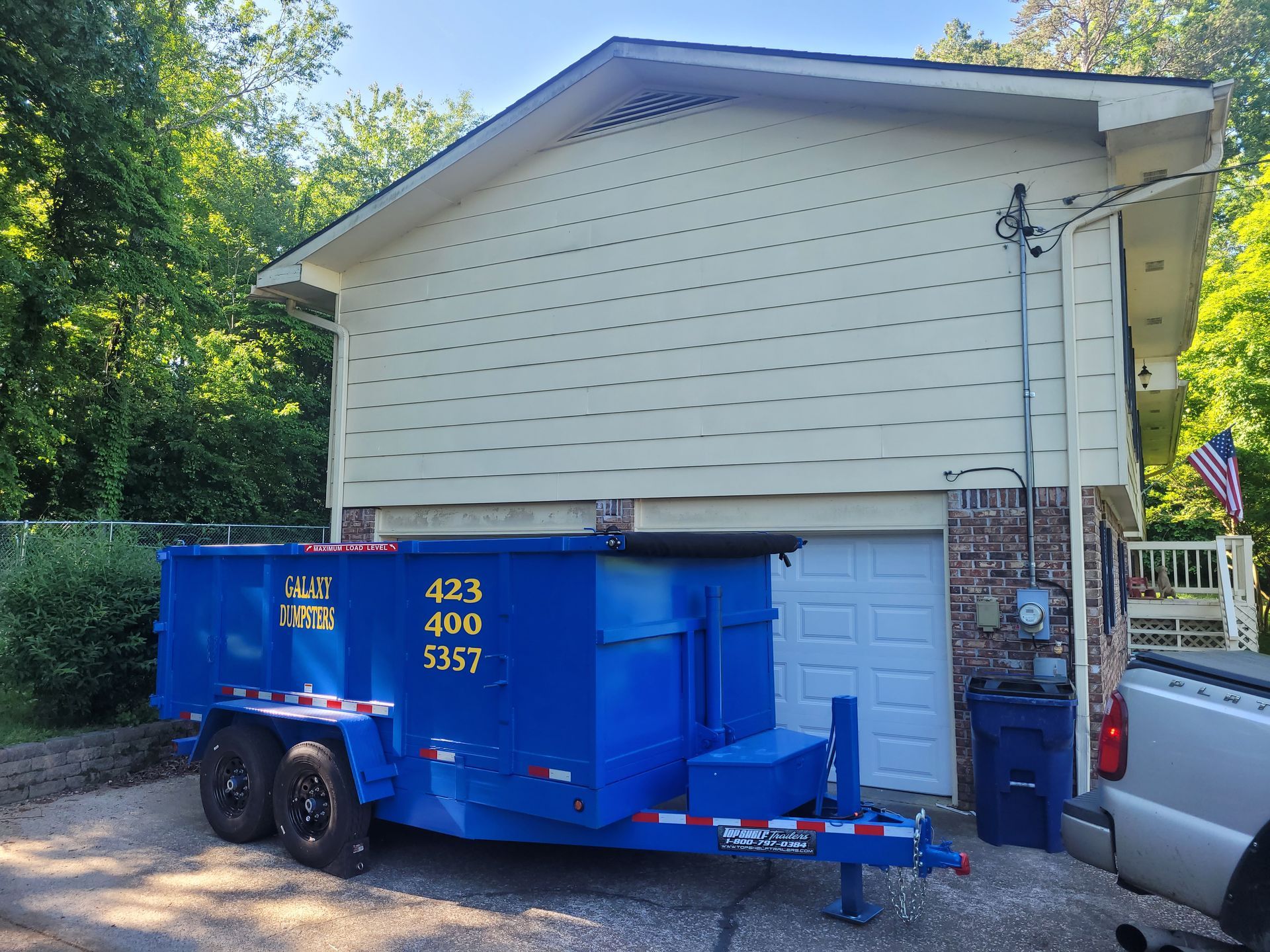 A blue dumpster is parked in front of a house.