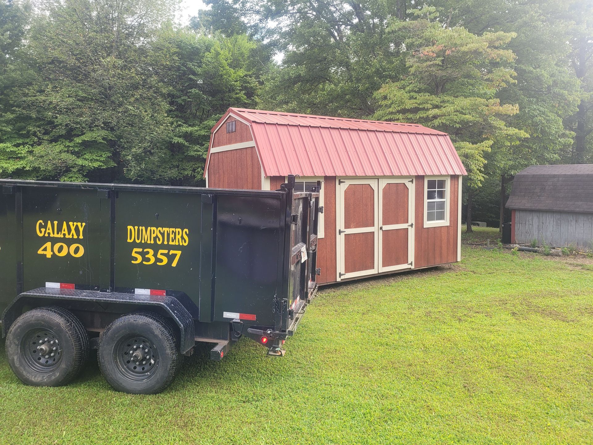 A dumpster is parked next to a barn in a grassy field.