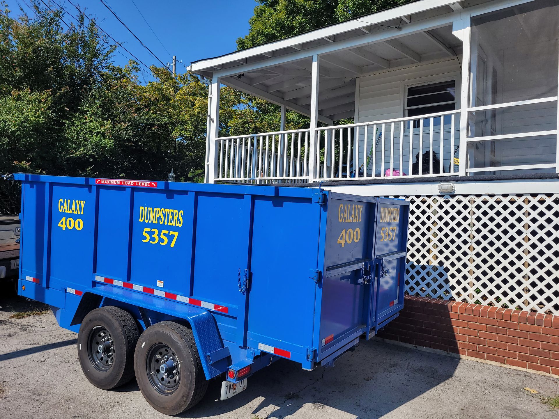 A blue dumpster is parked in front of a house.