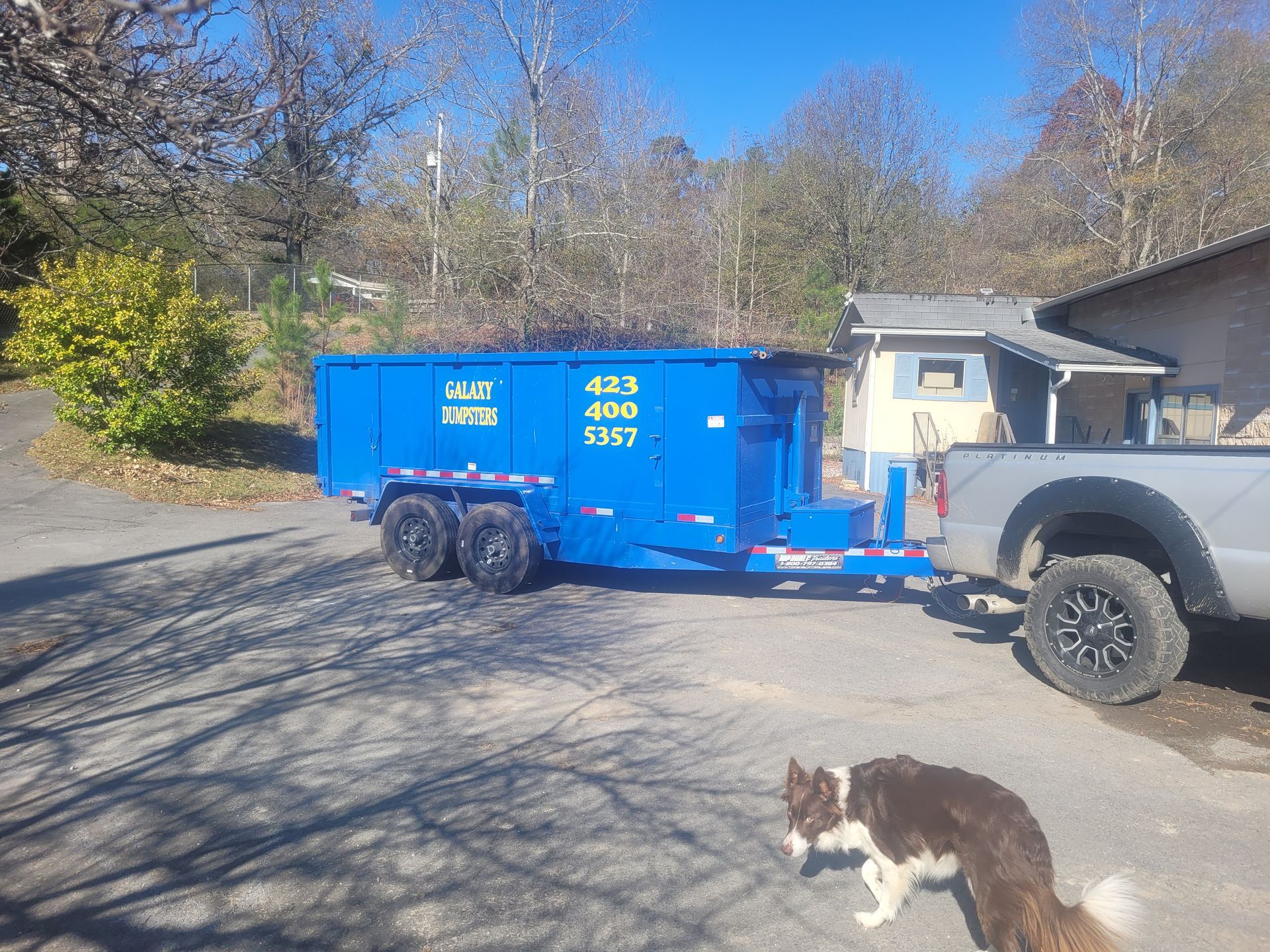 A blue dumpster is being towed by a truck.