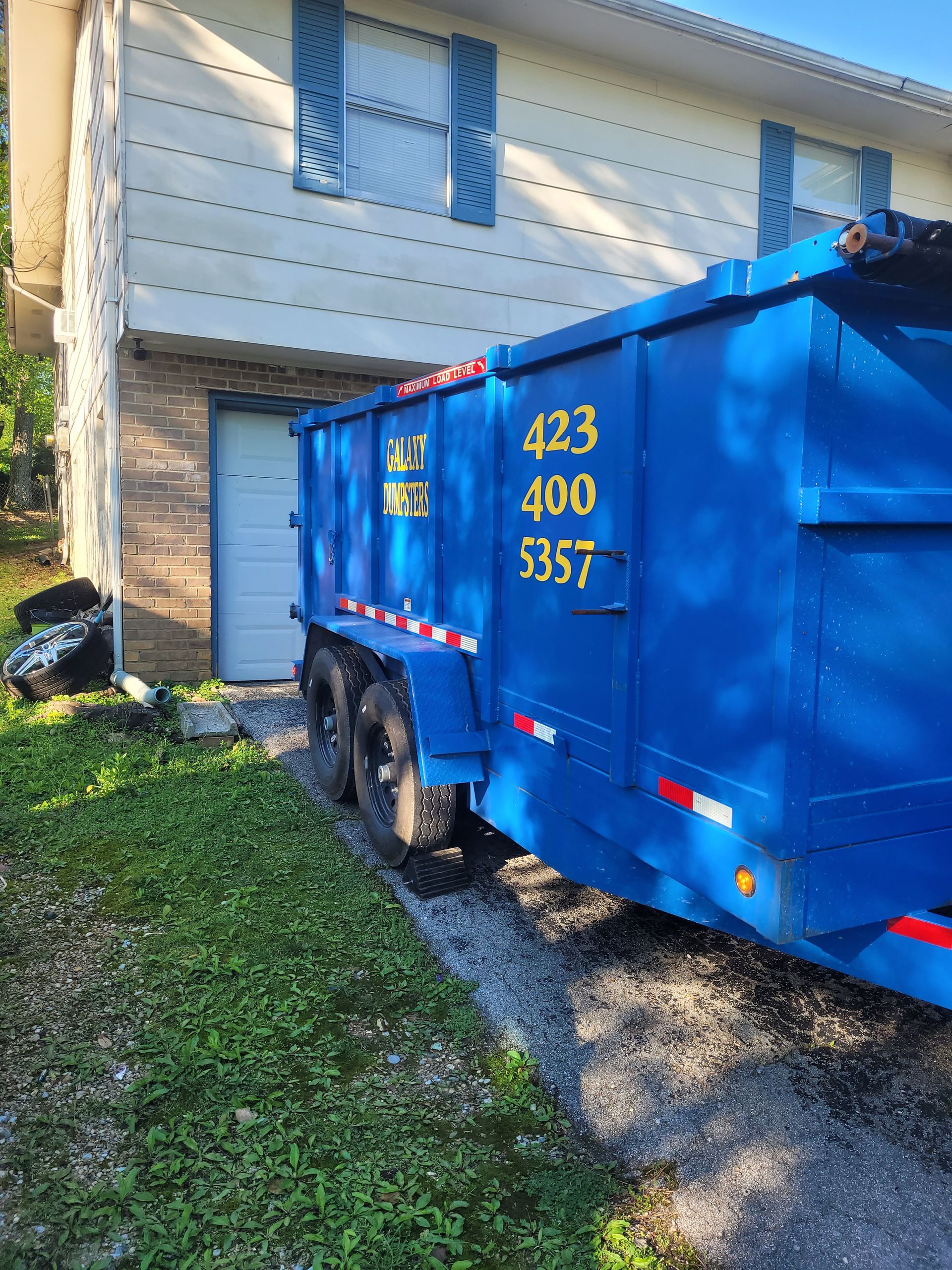 A blue dumpster is parked in front of a house.