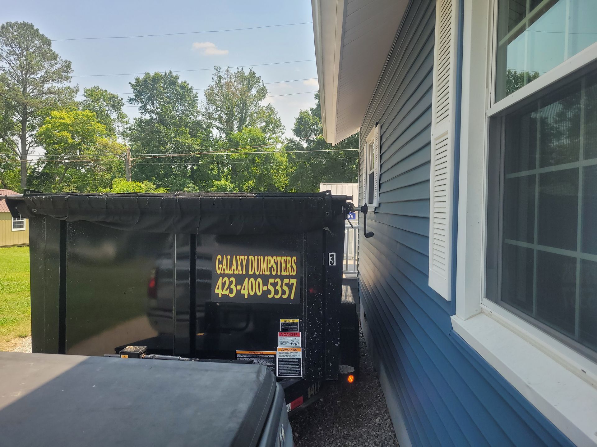A dumpster is parked in front of a blue house