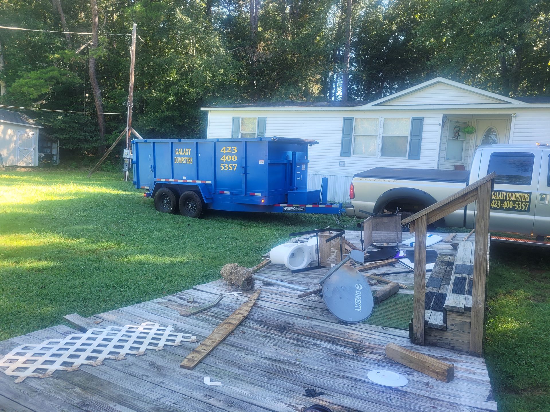 A blue dumpster is parked in front of a mobile home.