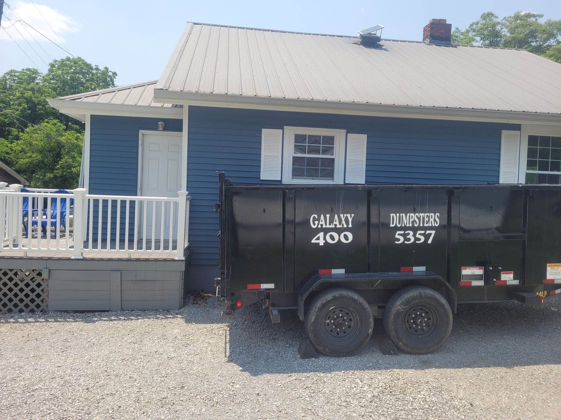 A black dumpster is parked in front of a blue house