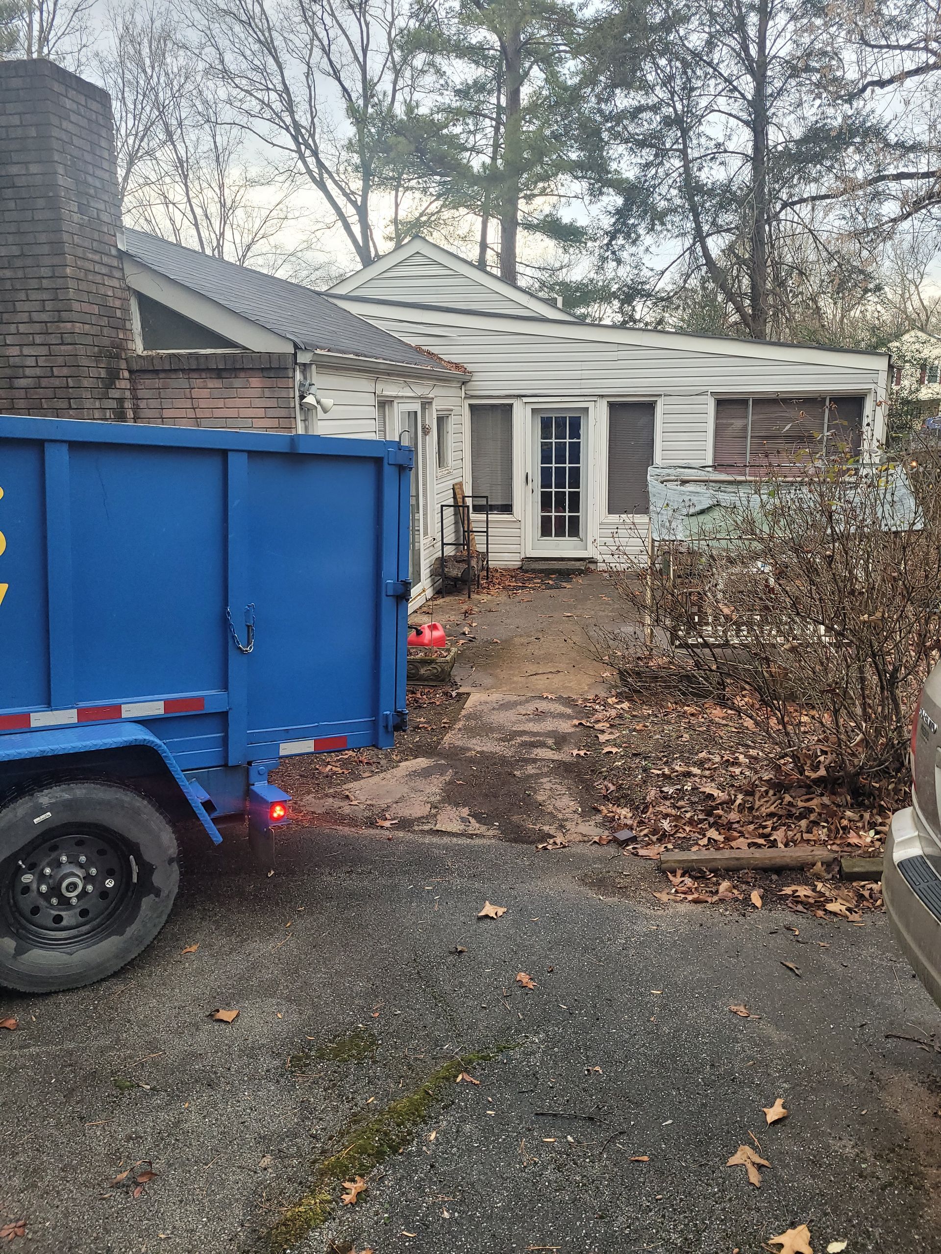 A blue dumpster is parked in front of a house.