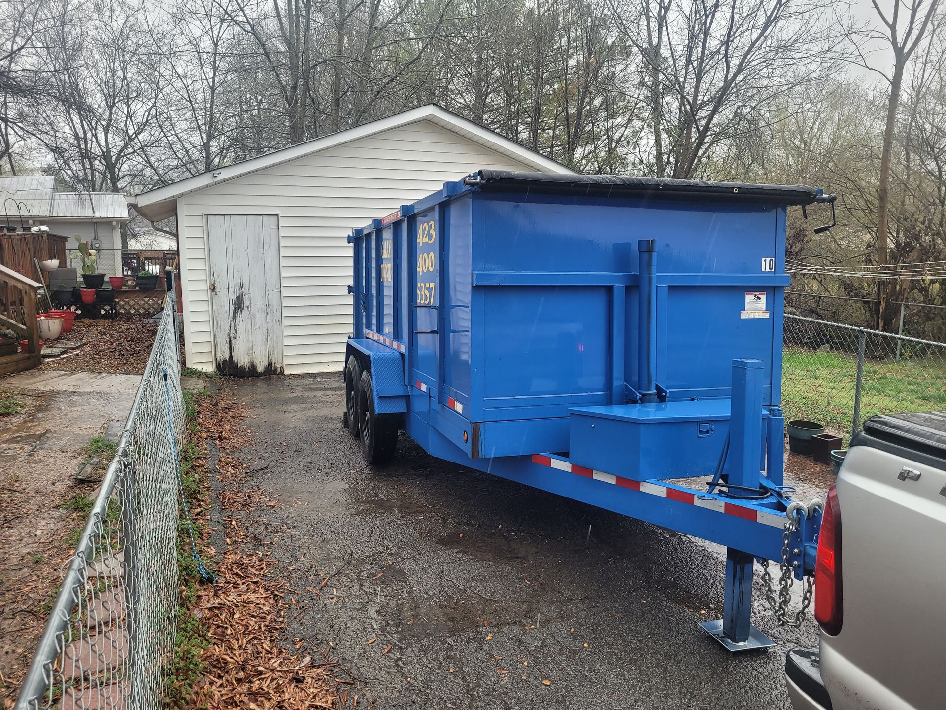 A blue dumpster trailer is parked in front of a white house.
