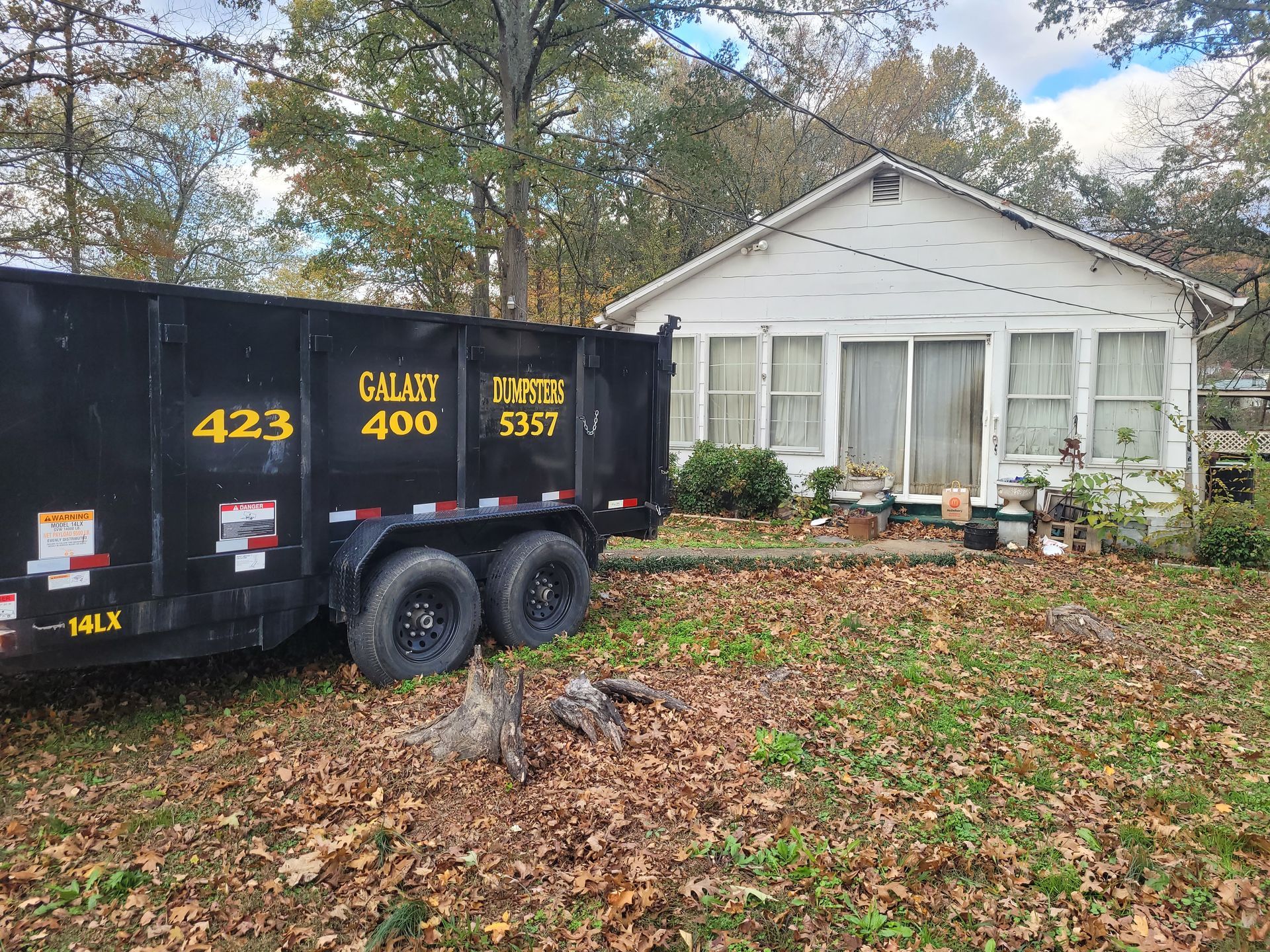 A dumpster is parked in front of a white house.