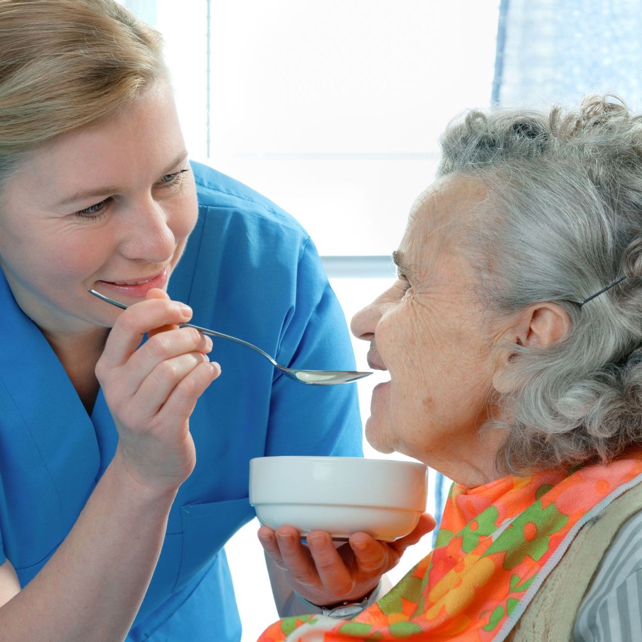 A nurse is feeding an elderly woman from a bowl with a spoon