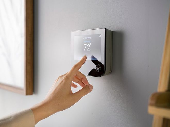 A person adjusting the settings on a wall-mounted thermostat in a modern, brightly lit home.