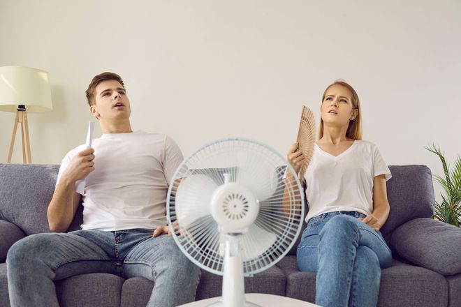 A professional in a blue uniform shakes hands with two people outside a home next to an HVAC outdoor unit.