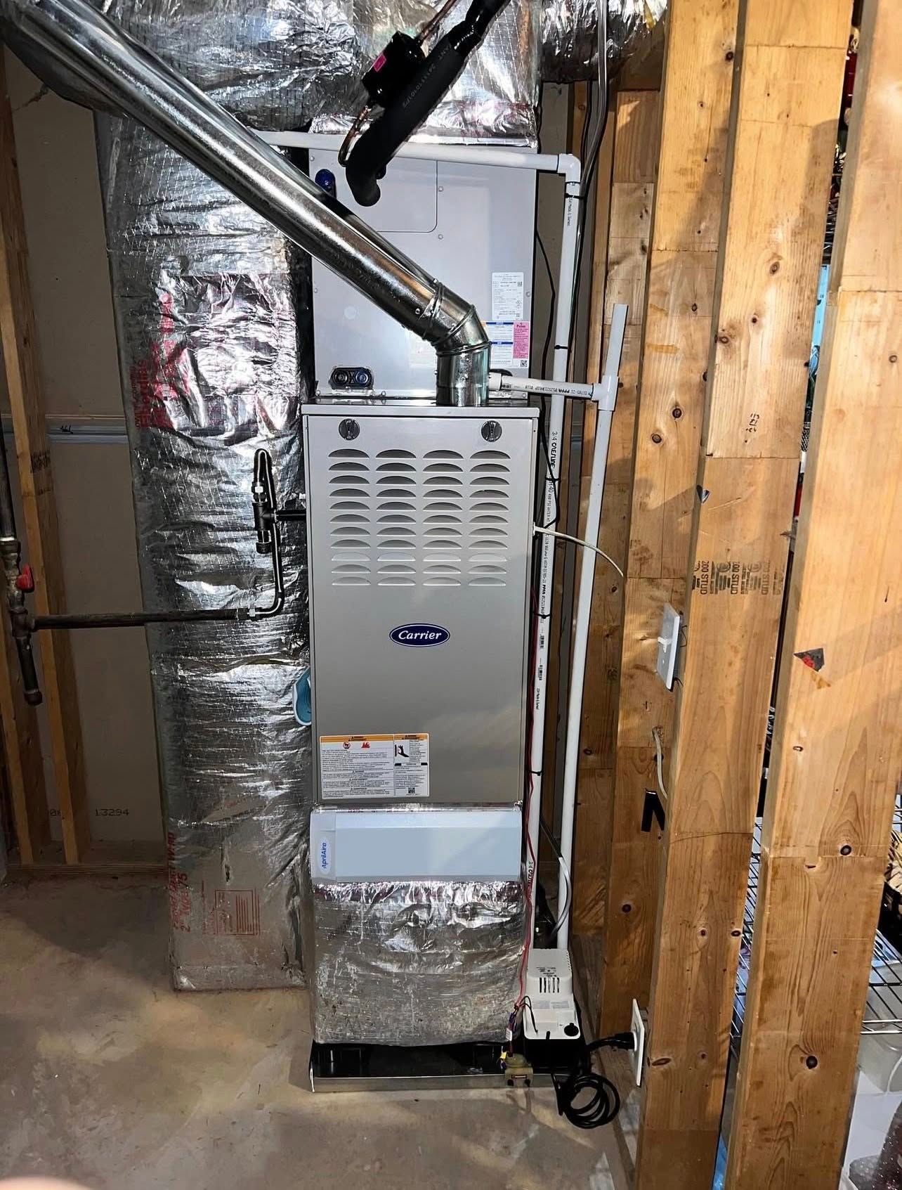 A silver gas furnace and ductwork installed in an unfinished basement with wooden wall studs.