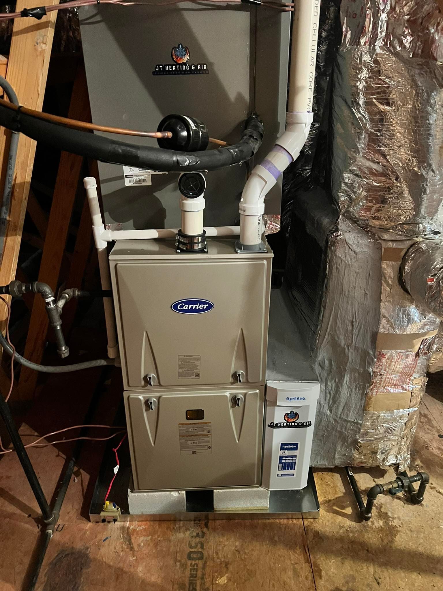 A modern HVAC furnace unit with silver panels and attached white PVC venting pipes in an attic setting.