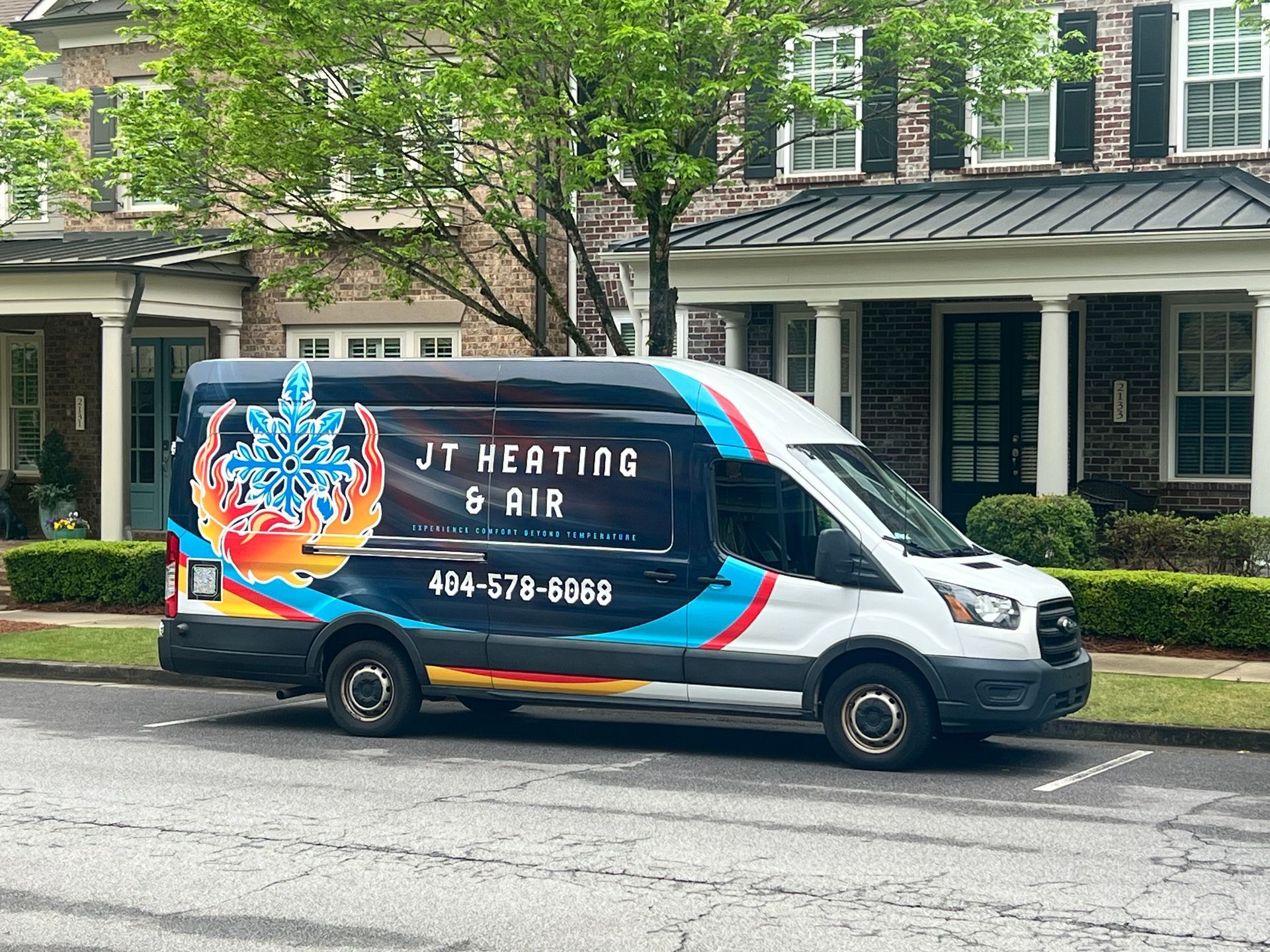 JT Heating & Air service van parked on a street in front of houses, with colorful flame graphics