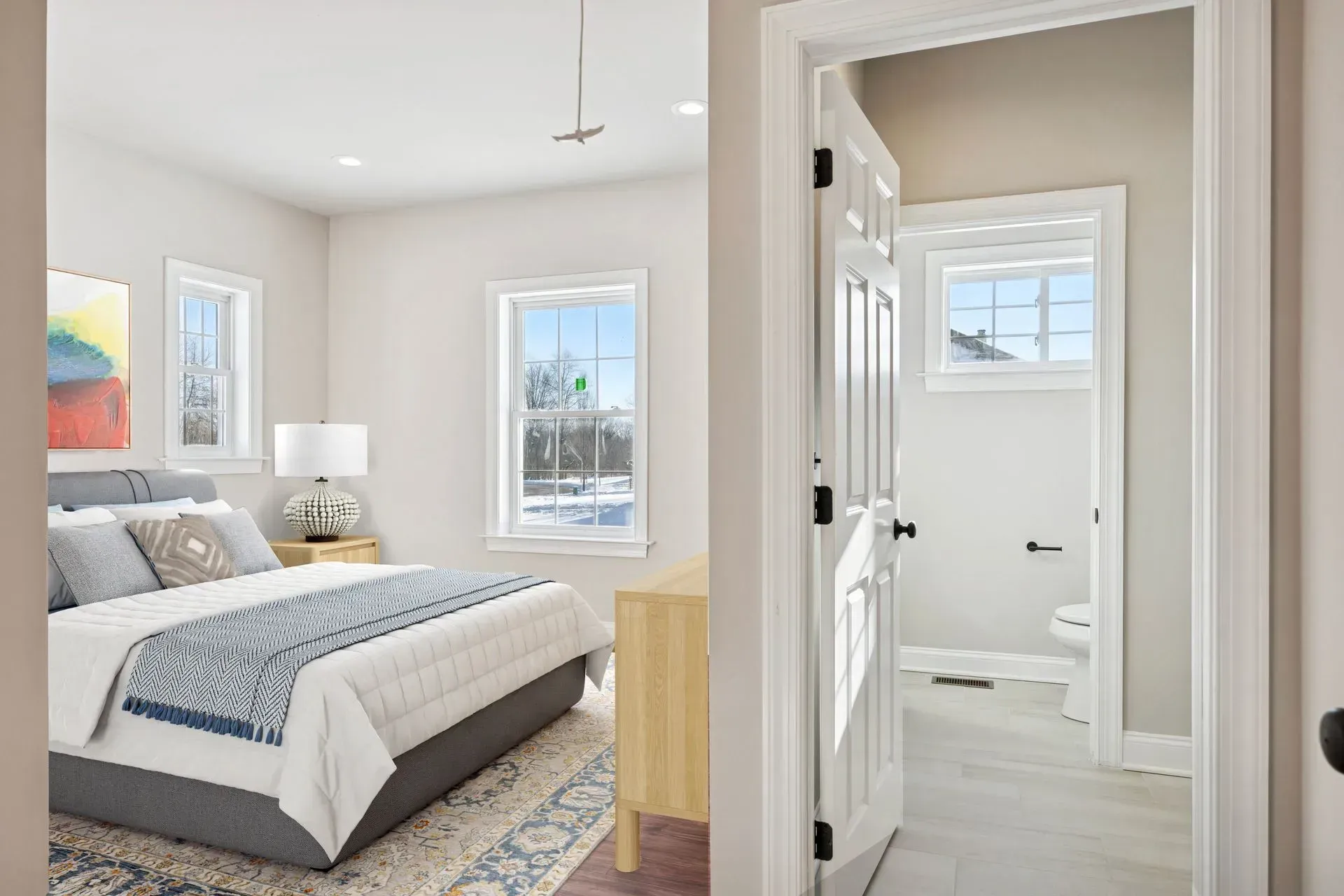 Bright bedroom with gray bed, patterned rug, and open doorway to a white bathroom