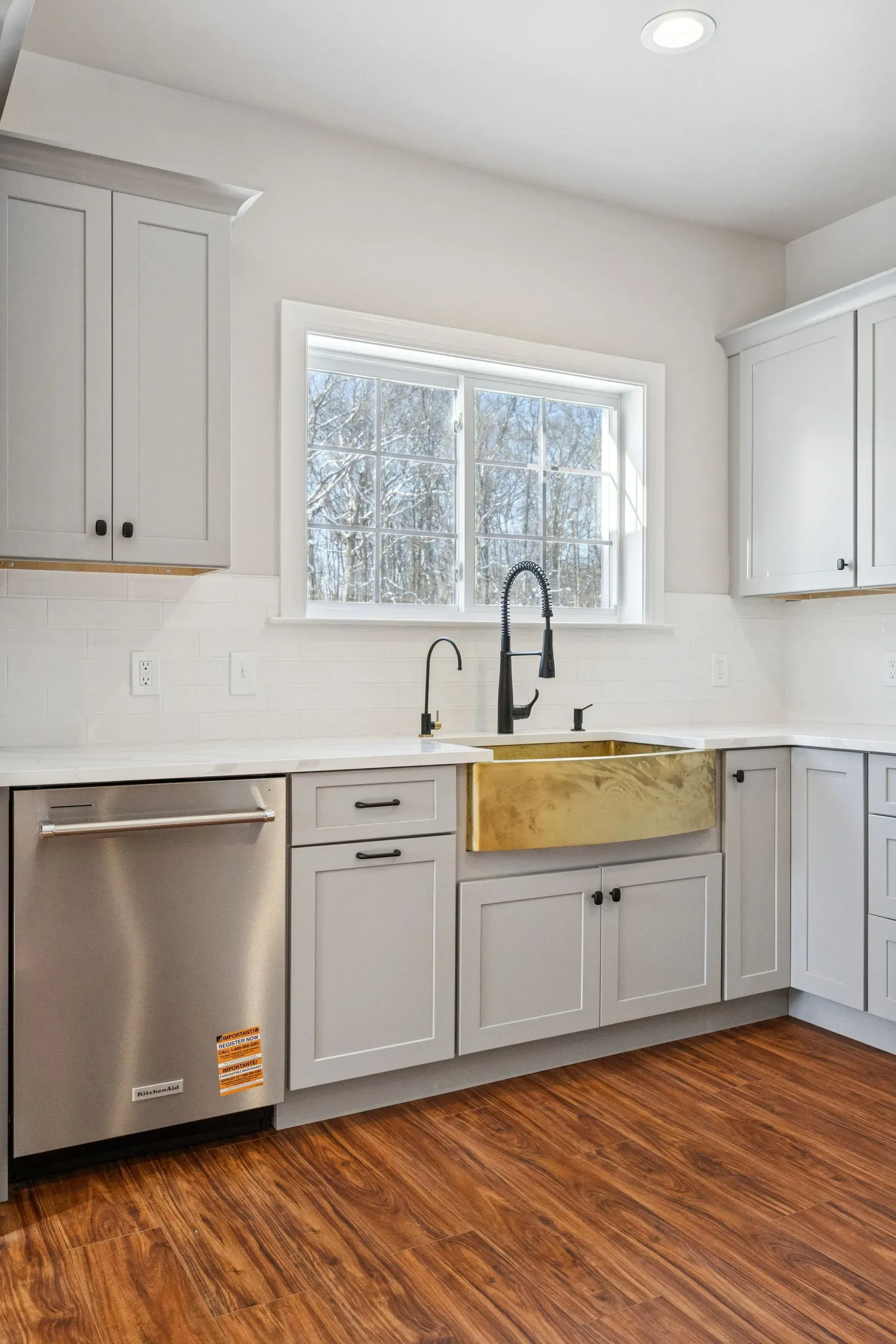 Modern white kitchen with stainless dishwasher, black faucet, and wood floor
