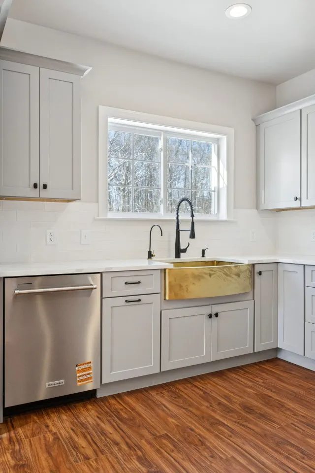 Modern kitchen with white cabinets, stainless dishwasher, black faucet, and a window over the sink.