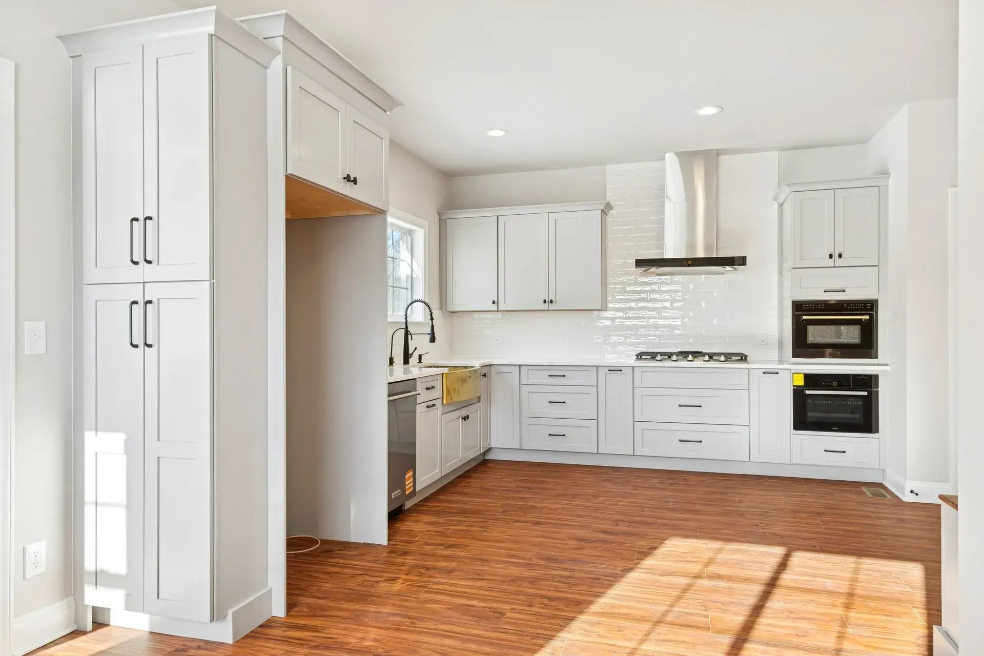 Bright white kitchen with stainless appliances, tiled backsplash, and warm wood floors