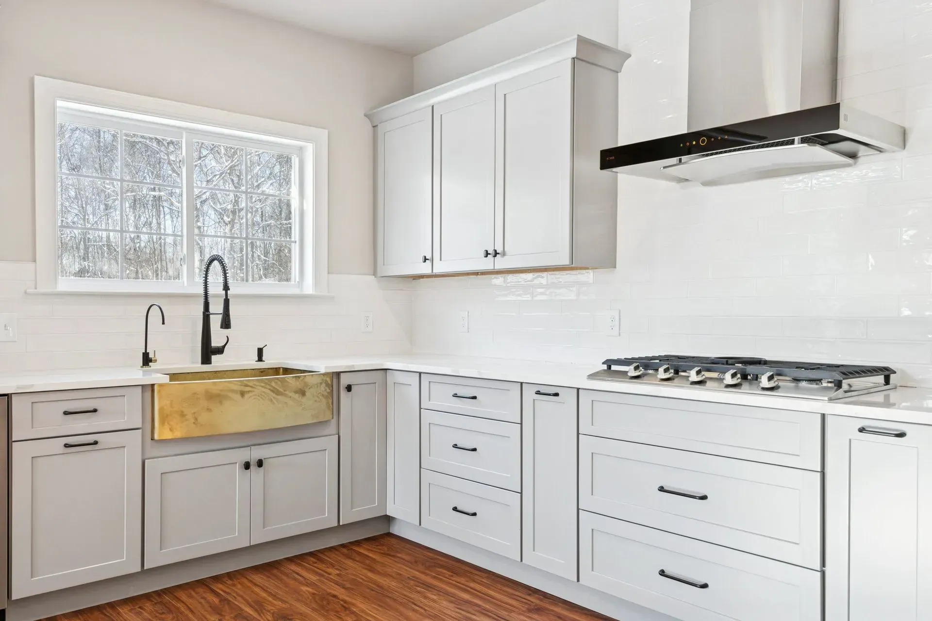 Bright modern kitchen with white cabinets, wood floor, marble backsplash, and a large farmhouse sink.